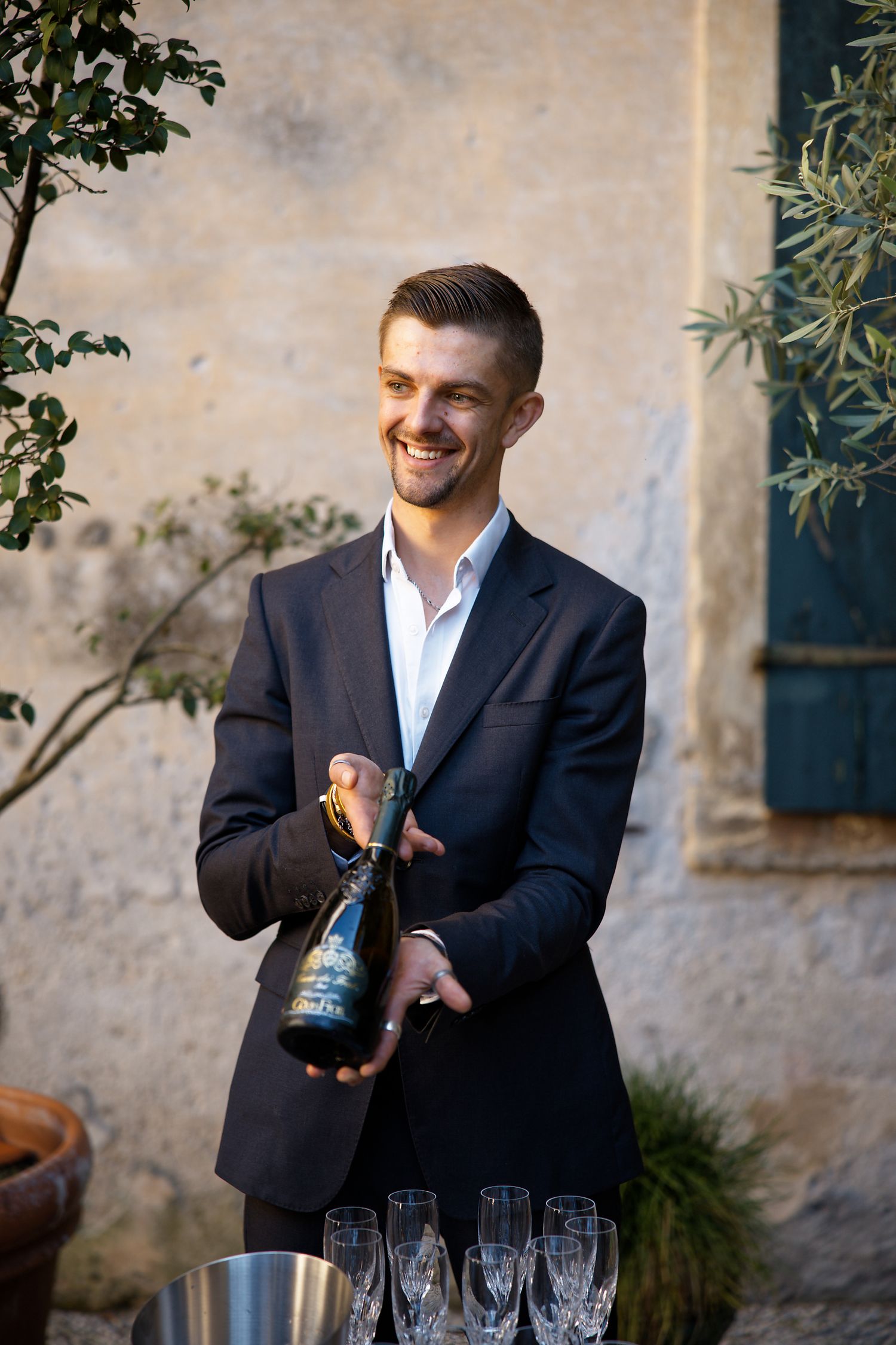 A gentleman in a dark suit pours champagne outdoors at an elegant event.