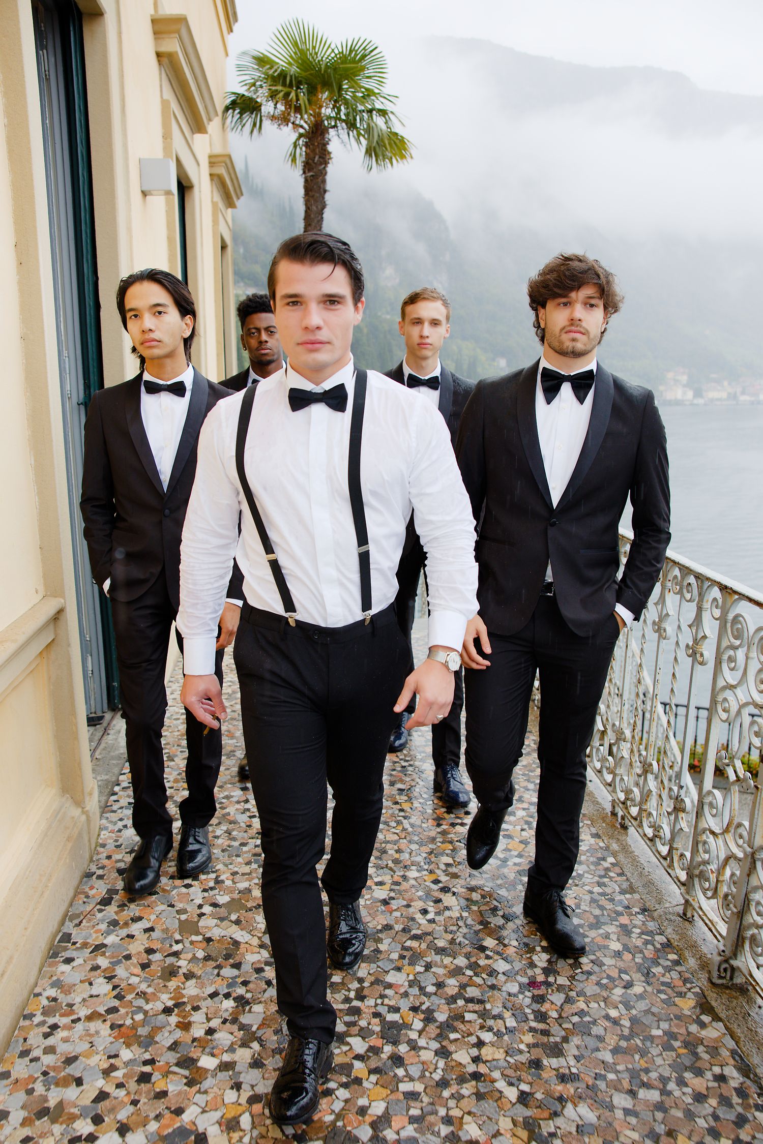 Groomsmen walking along a scenic balcony in formal suits and bowties.