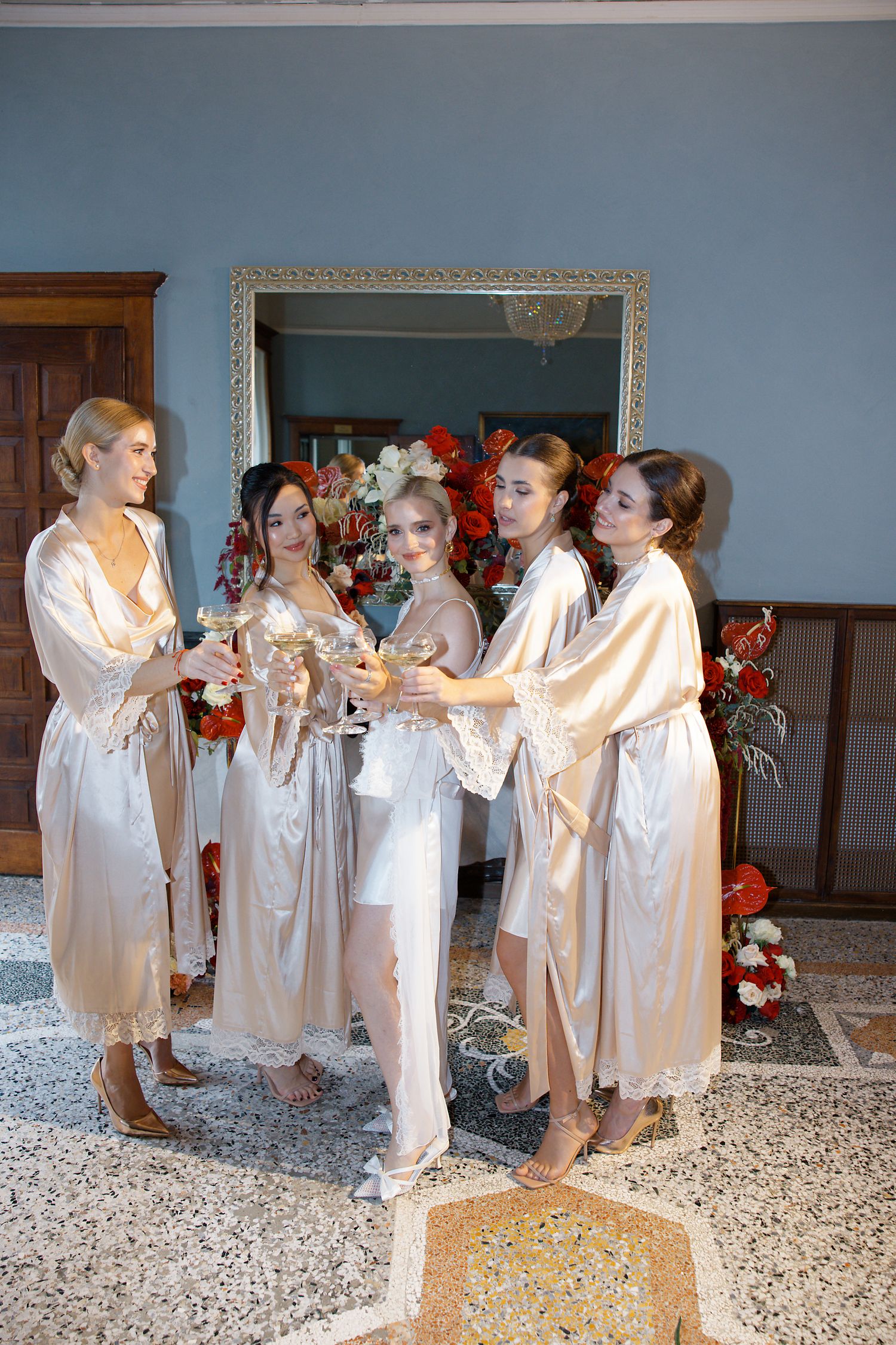 Bridesmaids in champagne-colored silk robes gather for a pre-wedding toast in an elegant room.