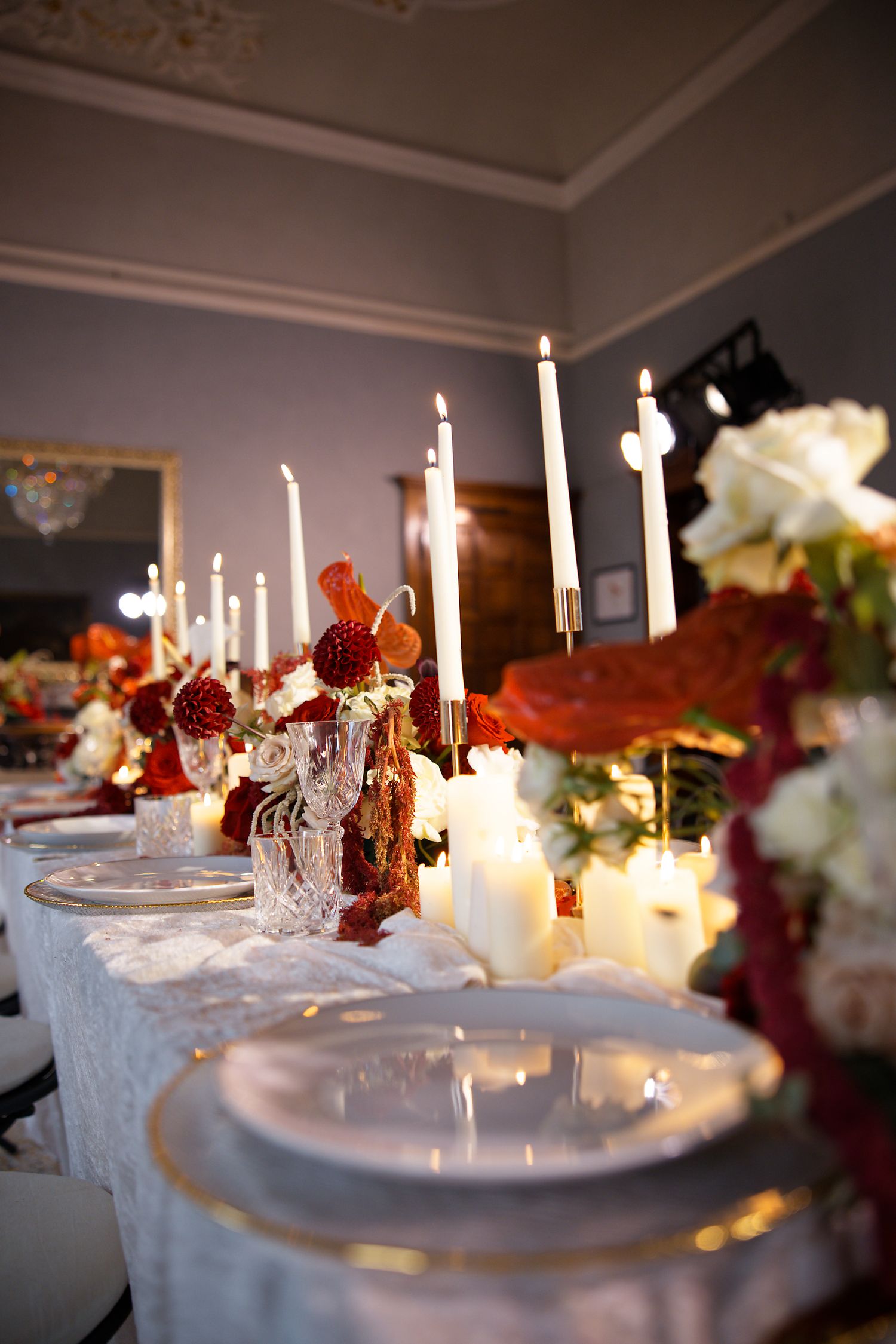 Elegant wedding table setting with white candles, white lace tablecloth, and floral arrangements in burgundy and white.