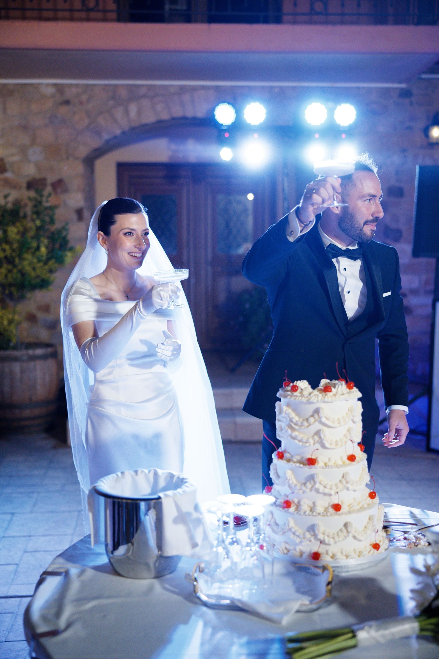 Happy couple celebrates by wedding cake with dramatic blue lighting at reception.