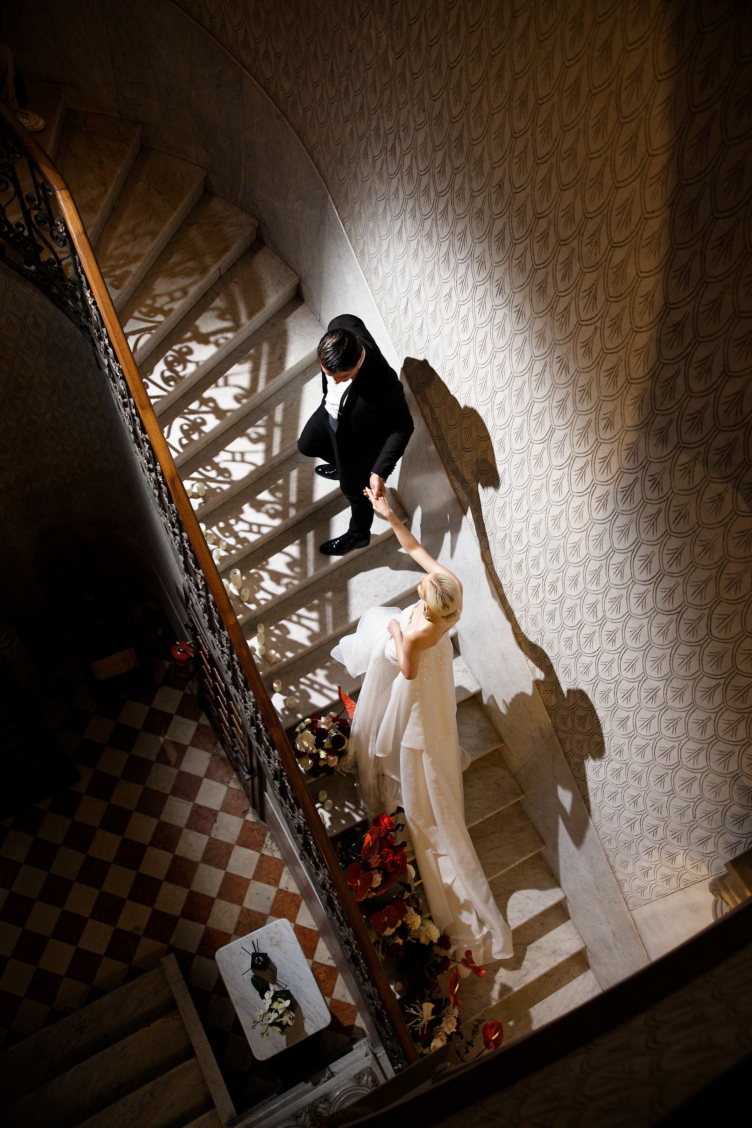 Dramatic black and white wedding photo on vintage staircase with shadows cast on textured wallpaper.