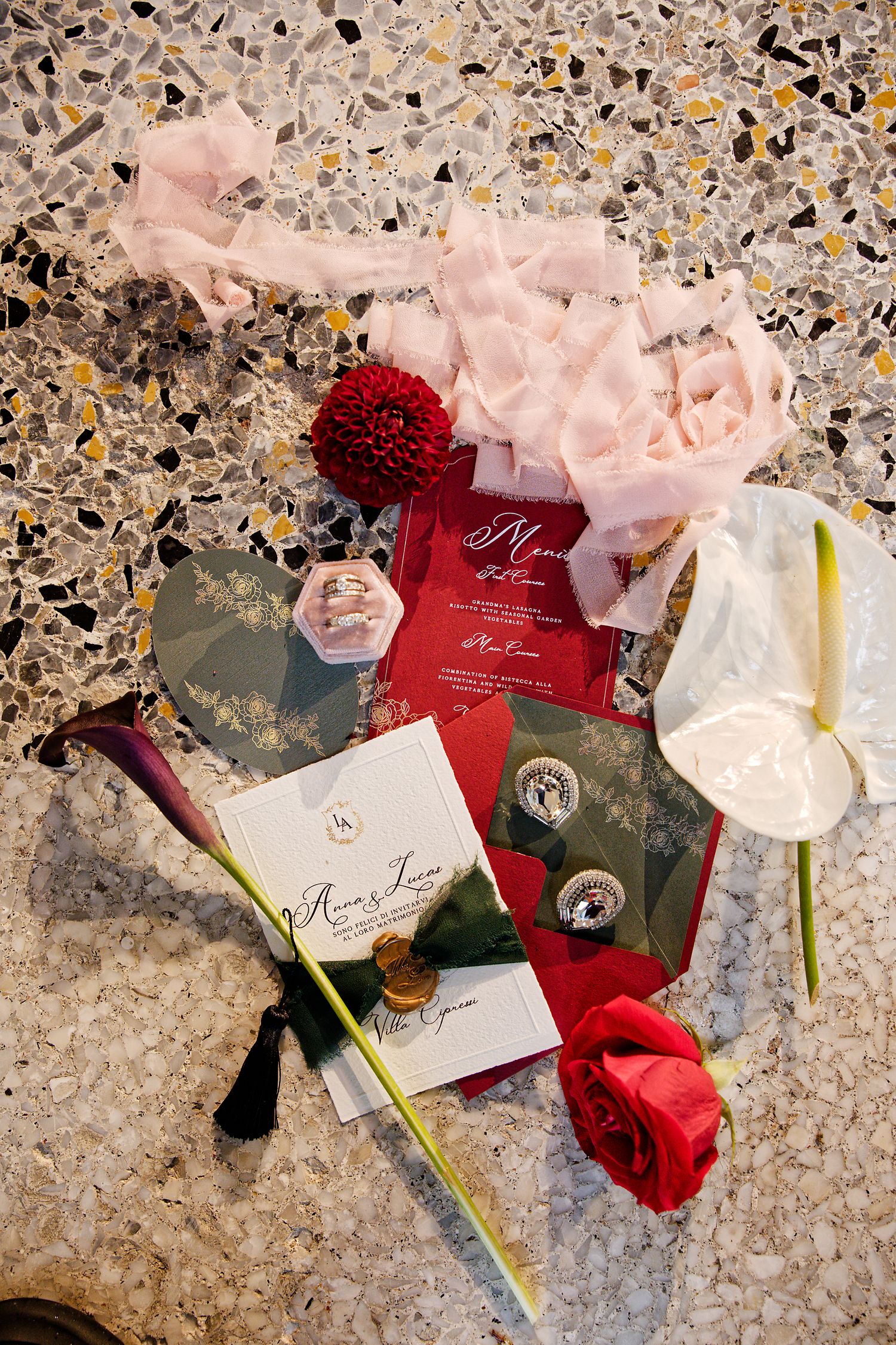 Wedding invitation suite with red and pink florals on terrazzo surface.