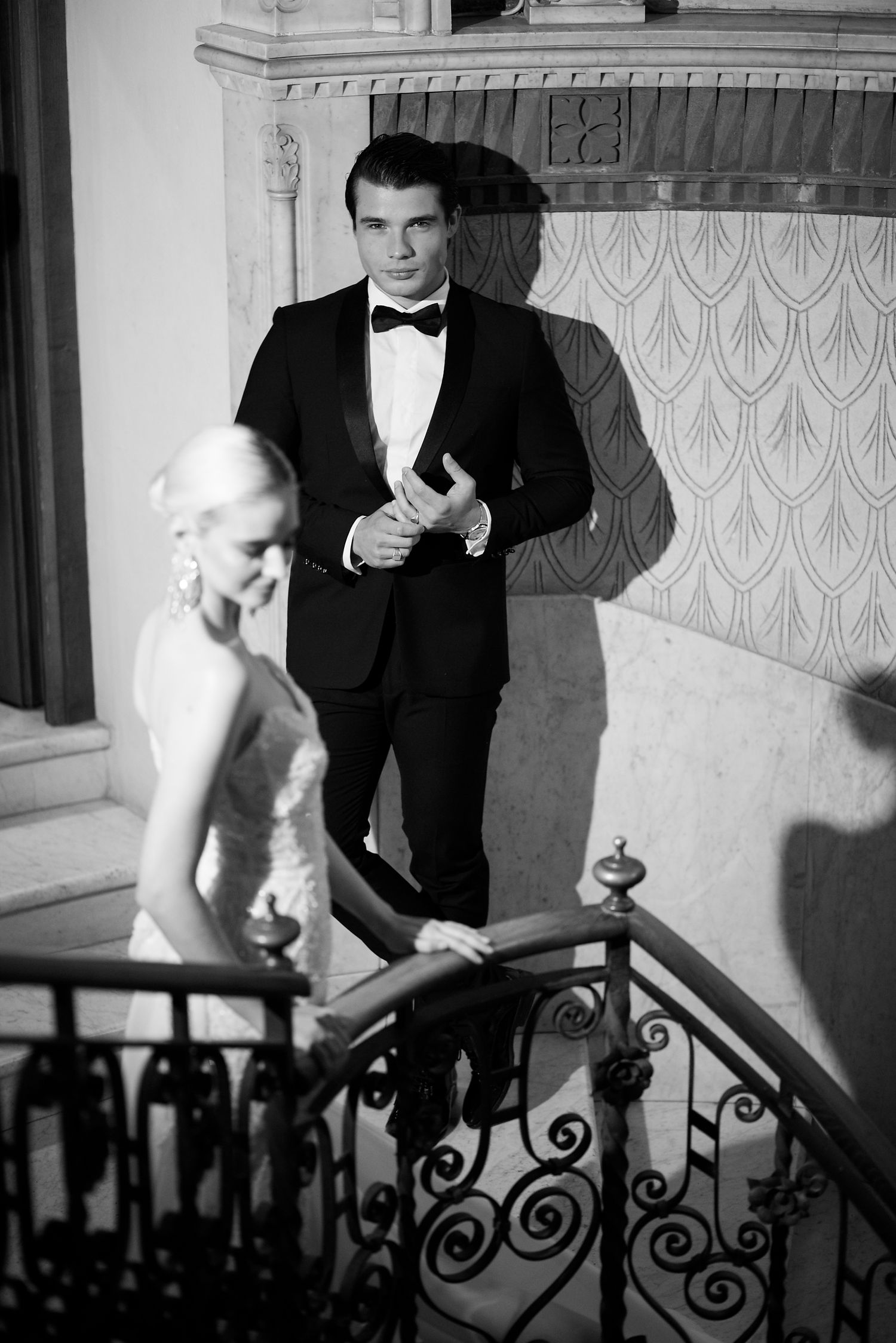 Black and white photo of formal couple on ornate staircase with wrought iron details.