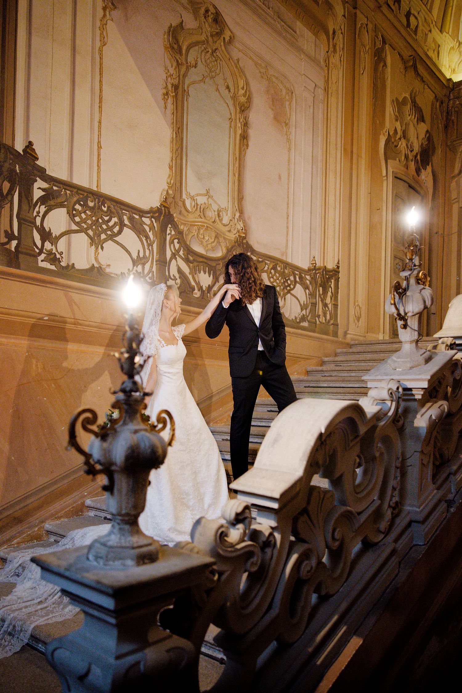 Newlyweds share an intimate moment on an elegant baroque staircase with ornate details.