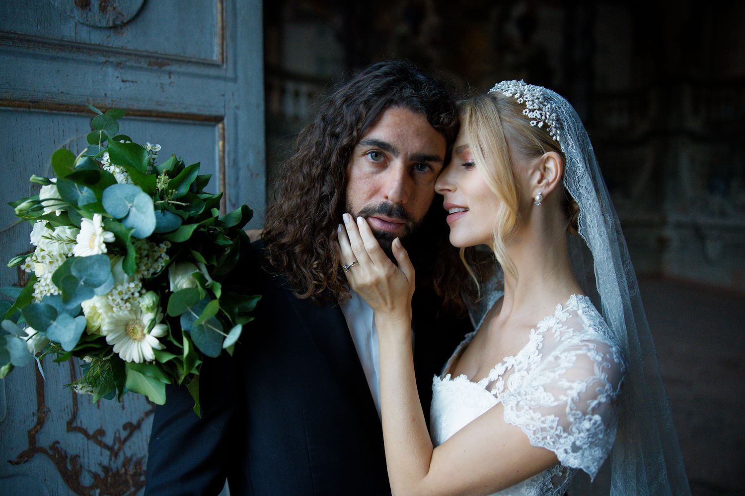 An intimate wedding moment captured against vintage blue doors with white floral decorations.