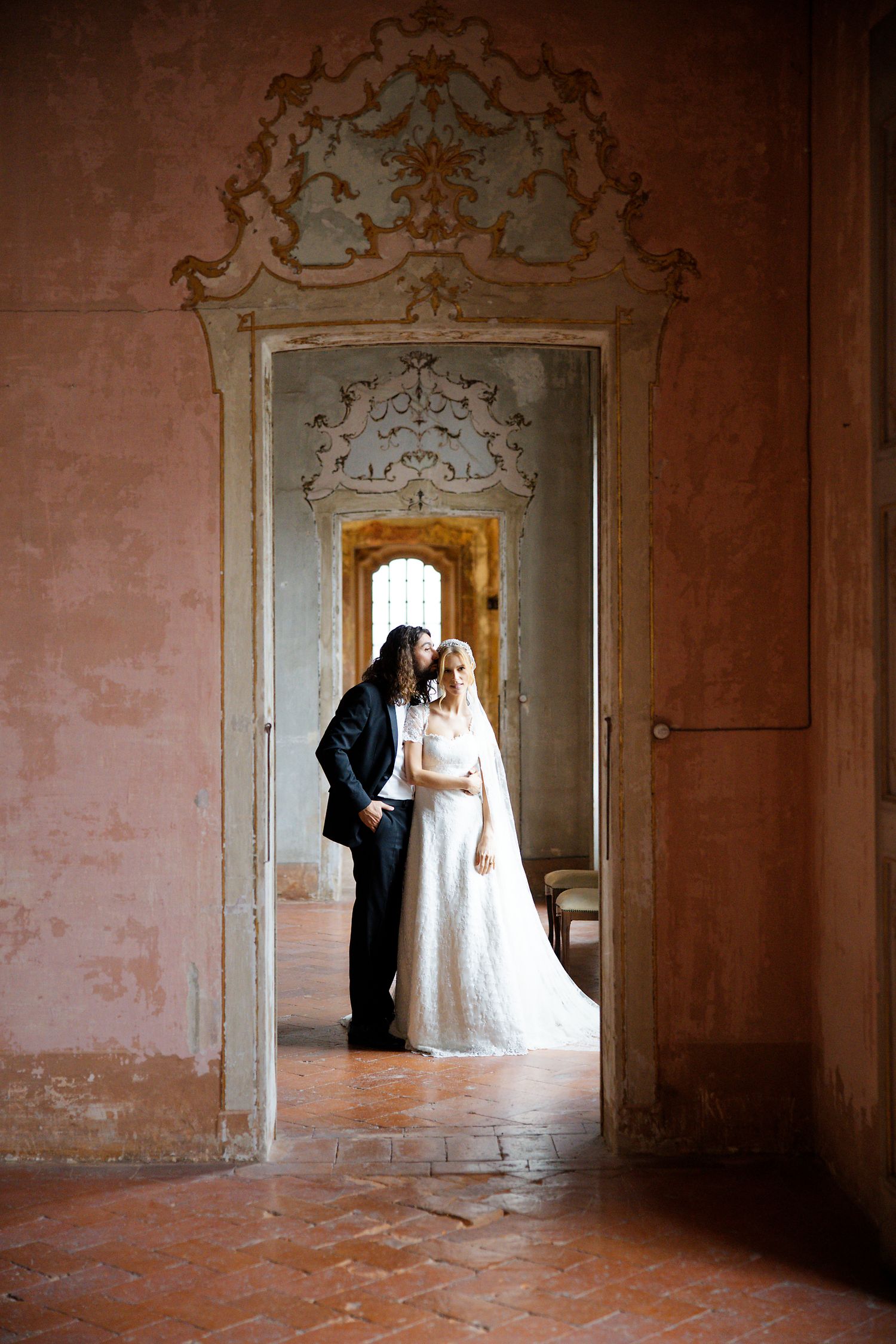 A romantic wedding photo showing silhouettes through an ornate doorway in a historic building.