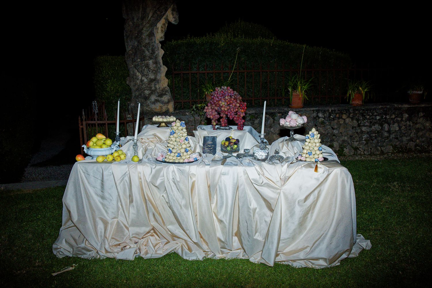 Elegant wedding dessert table with white tablecloth and floral decorations at night.