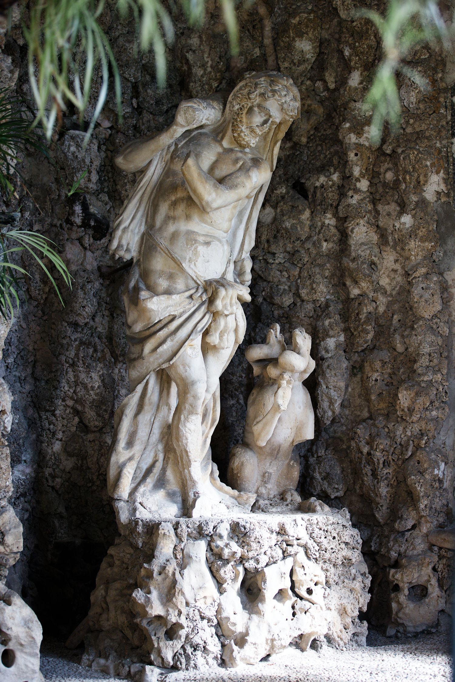 Classical stone statues nestled in a garden grotto with hanging vines and natural rock formations.