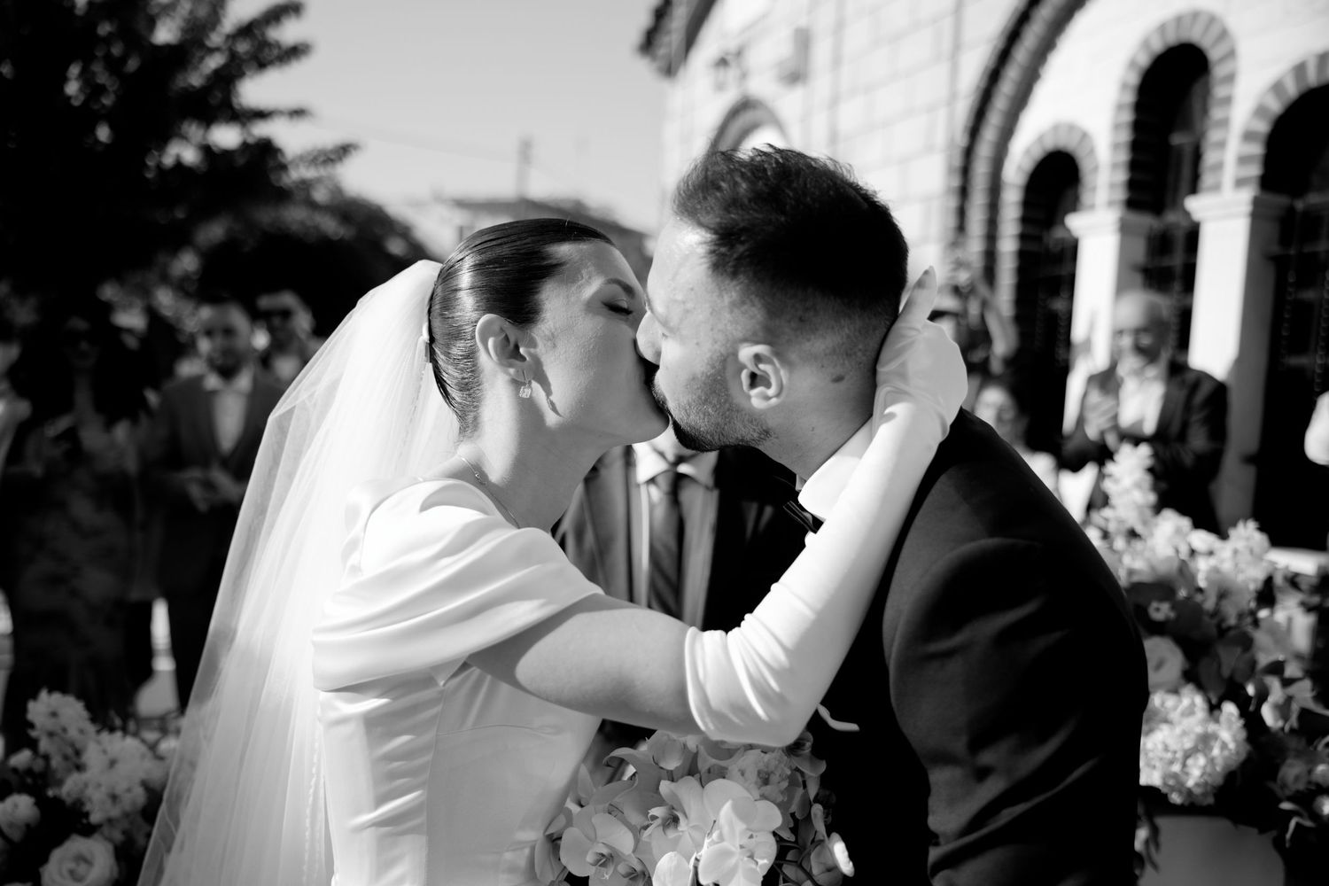 Intimate moment between newlyweds sharing their first kiss under an ornate archway.