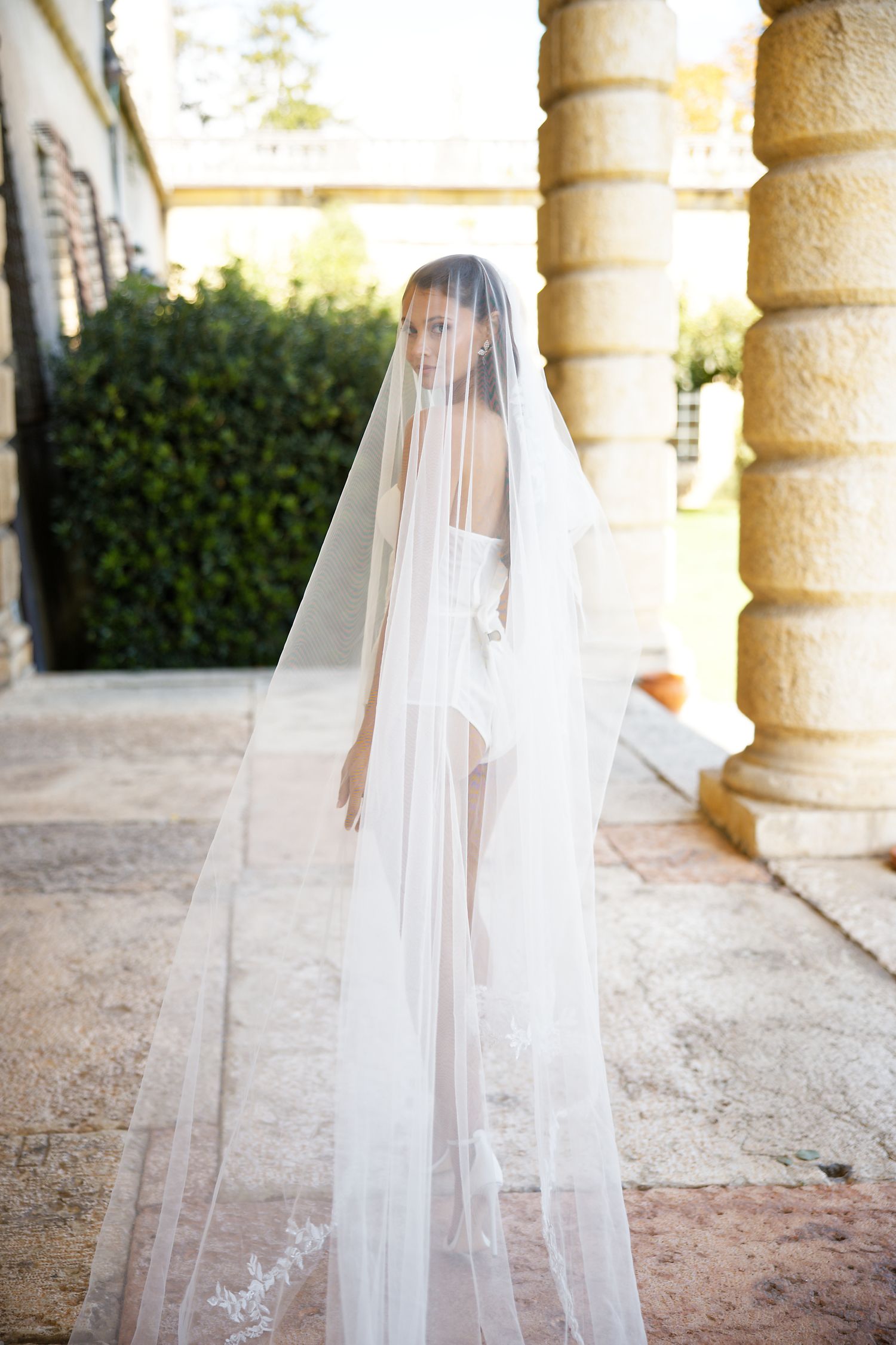 Ethereal bridal portrait with flowing cathedral veil in stone colonnade setting.
