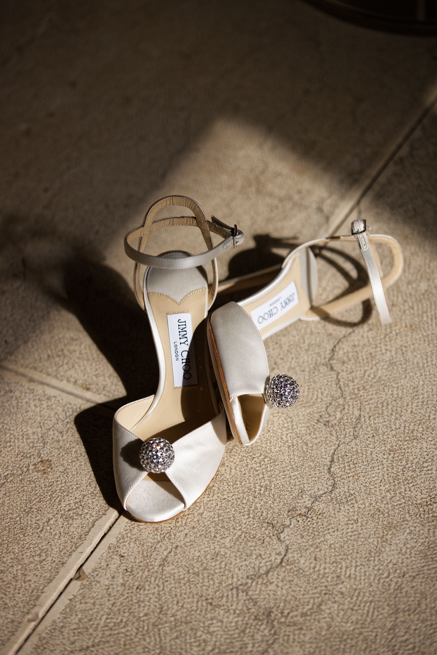 Elegant white Jimmy Choo bridal shoes with crystal embellishments photographed in dramatic lighting.