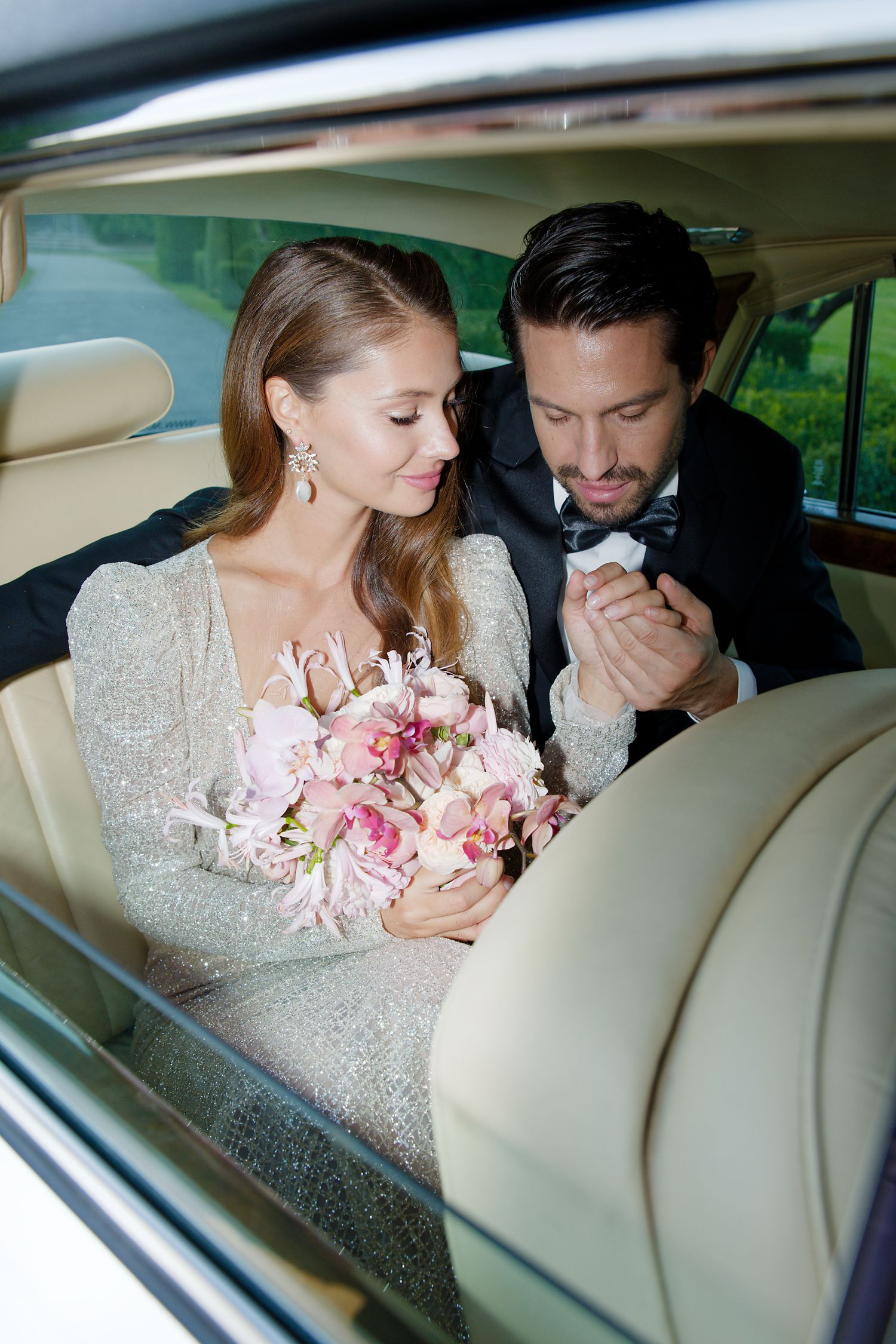 Romantic moment captured in luxury car backseat with pink bridal bouquet.