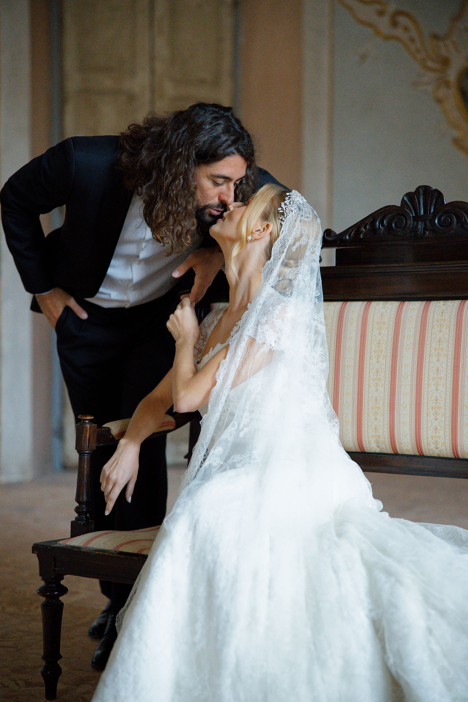 A romantic wedding moment captured in an elegant interior with vintage furniture and ornate details.