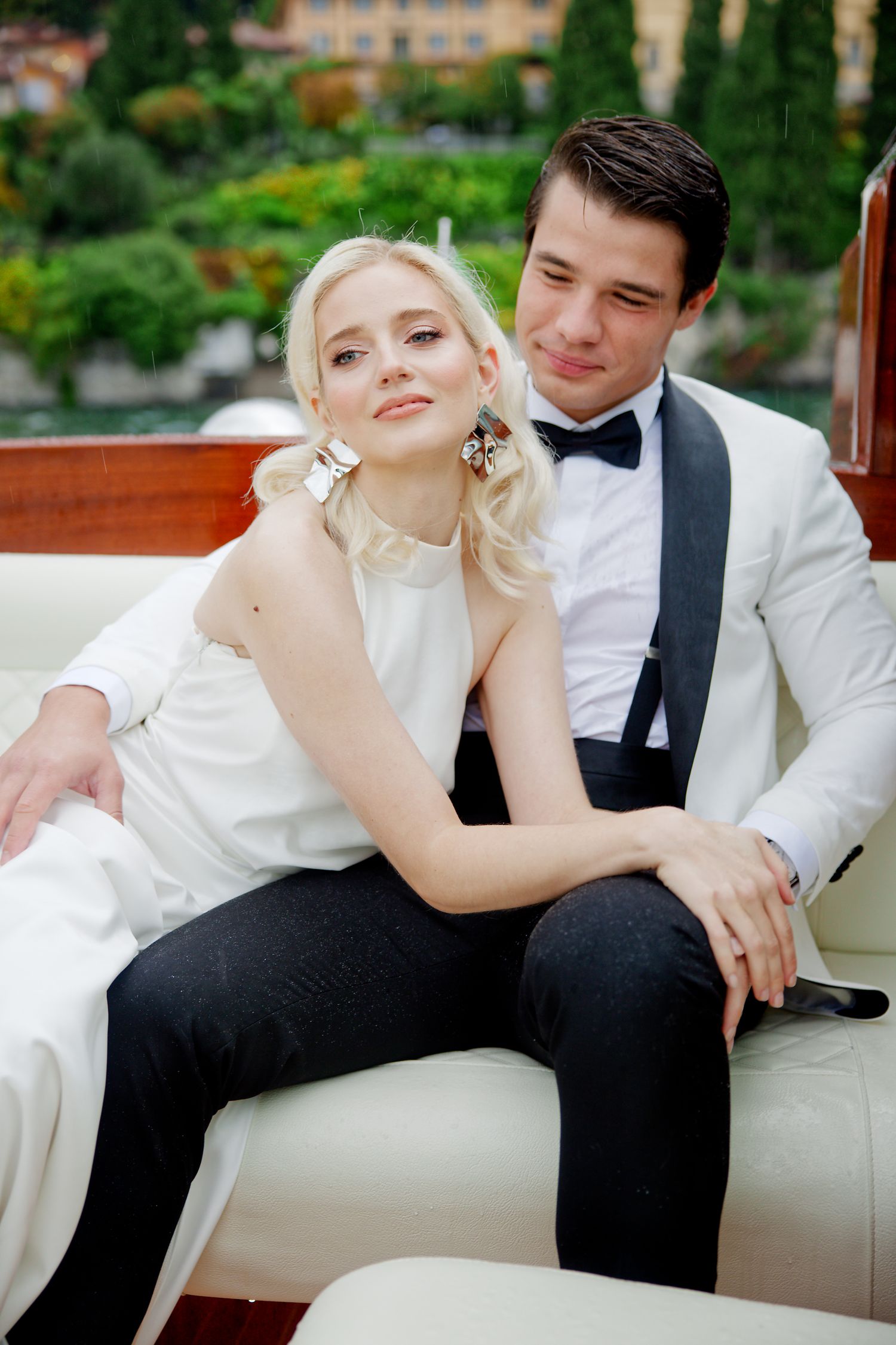 A romantic couple in wedding attire cuddles on a luxury boat with scenic Italian views in the background.