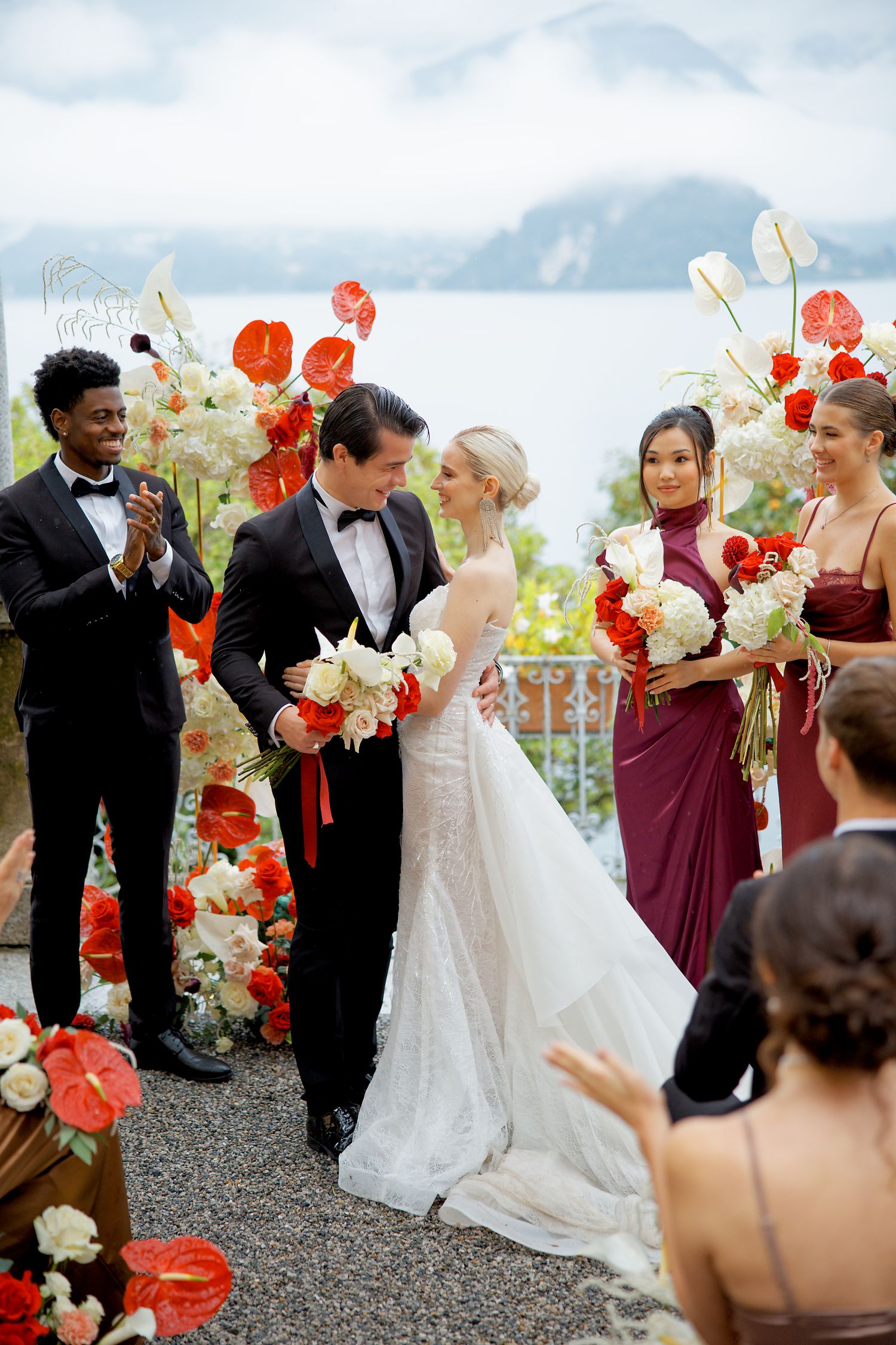 An outdoor wedding ceremony with coral and white floral arrangements against a mountain backdrop.