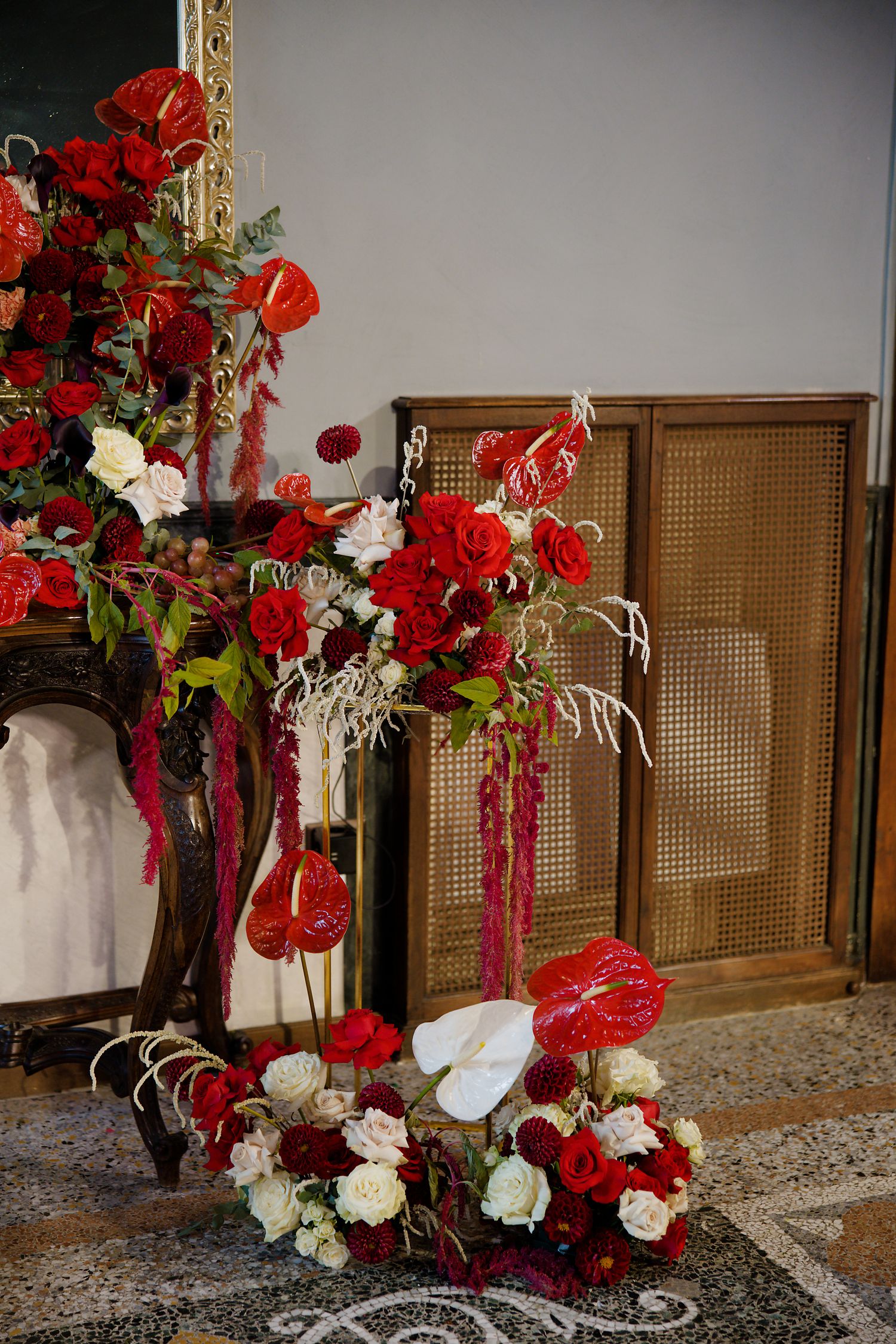 Dramatic floral arrangement with red and white flowers against wooden screen backdrop.
