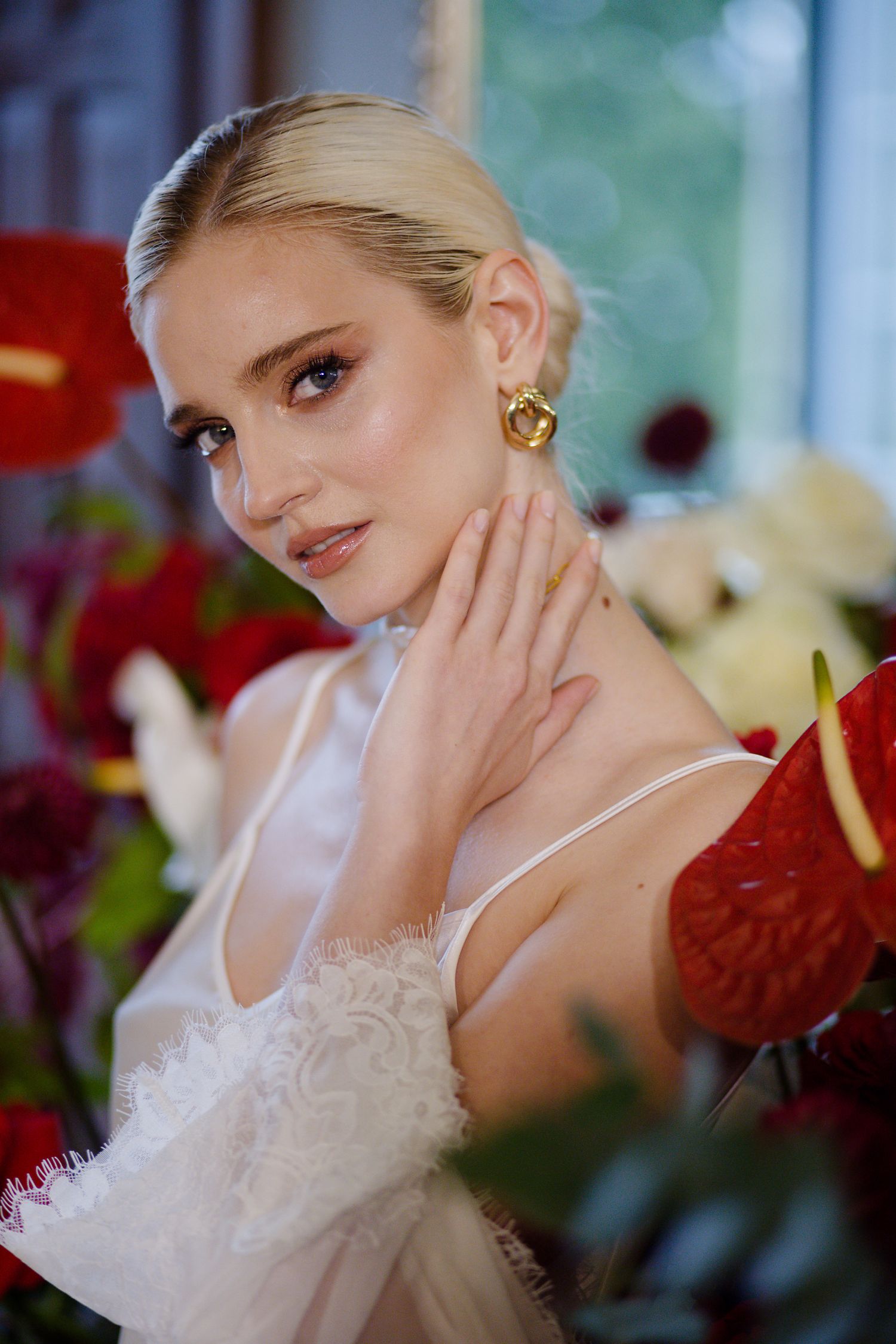 Bridal portrait with delicate jewelry and white dress against red flower backdrop.