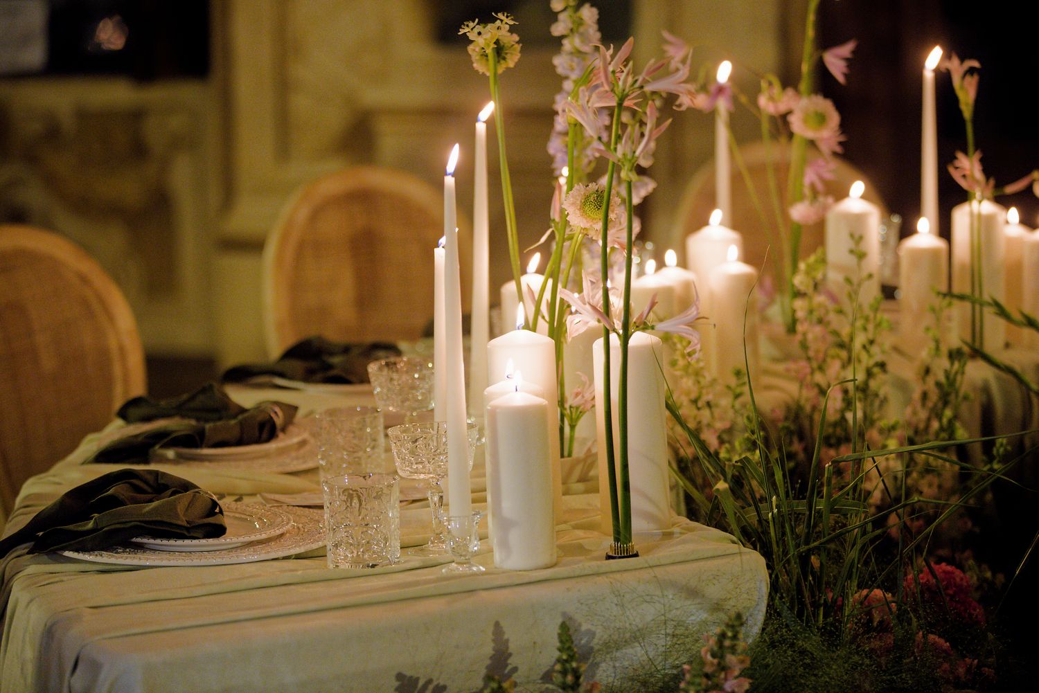 Romantic table setting with tall candles and pink floral arrangements at elegant dinner.