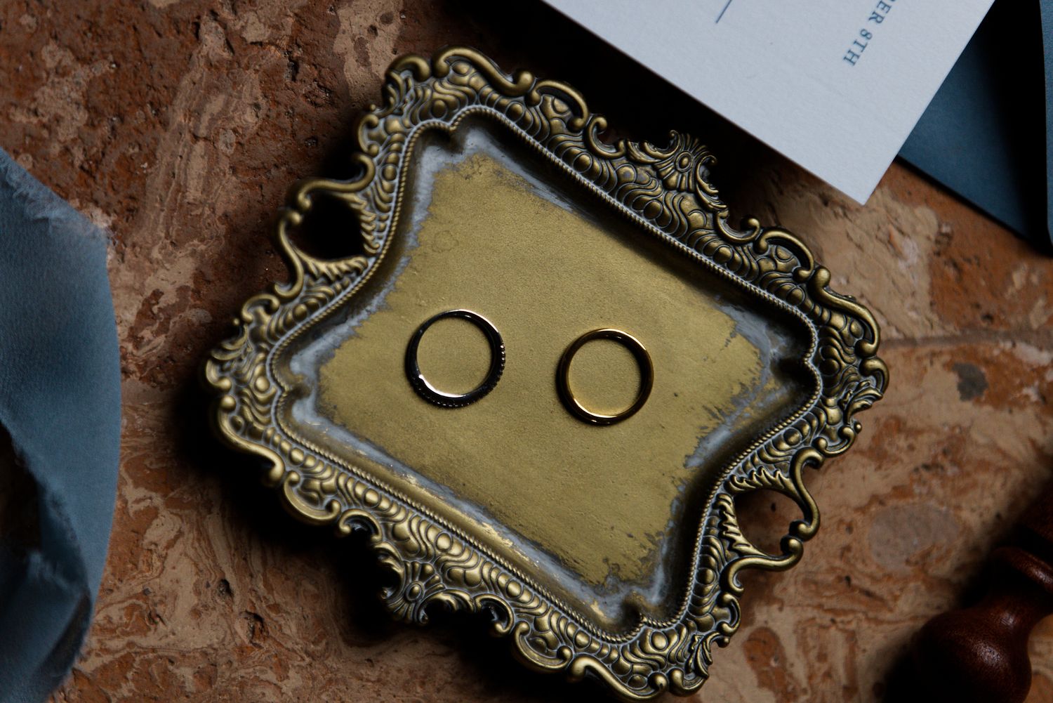 Wedding rings displayed in an ornate vintage gold frame on a textured brown surface.