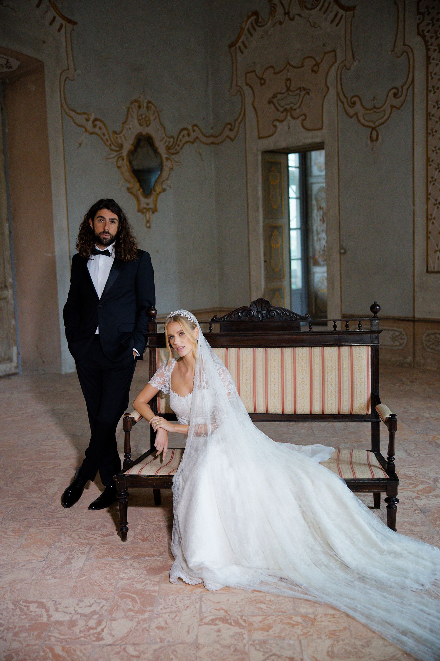 A romantic wedding photo in an ornate vintage room with a couple posing on an antique bench.