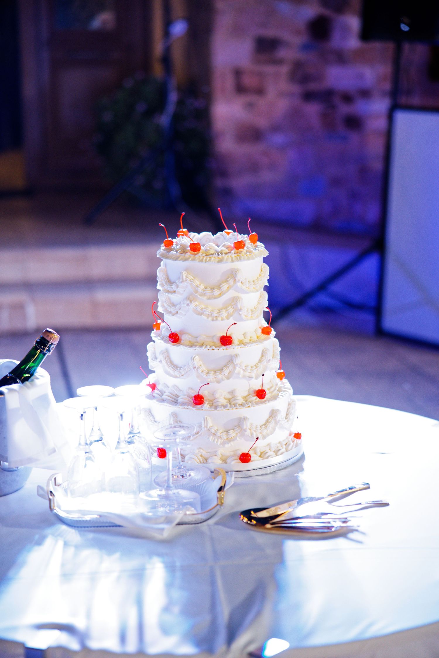 A white three-tiered wedding cake with red cherry decorations displayed on a table.