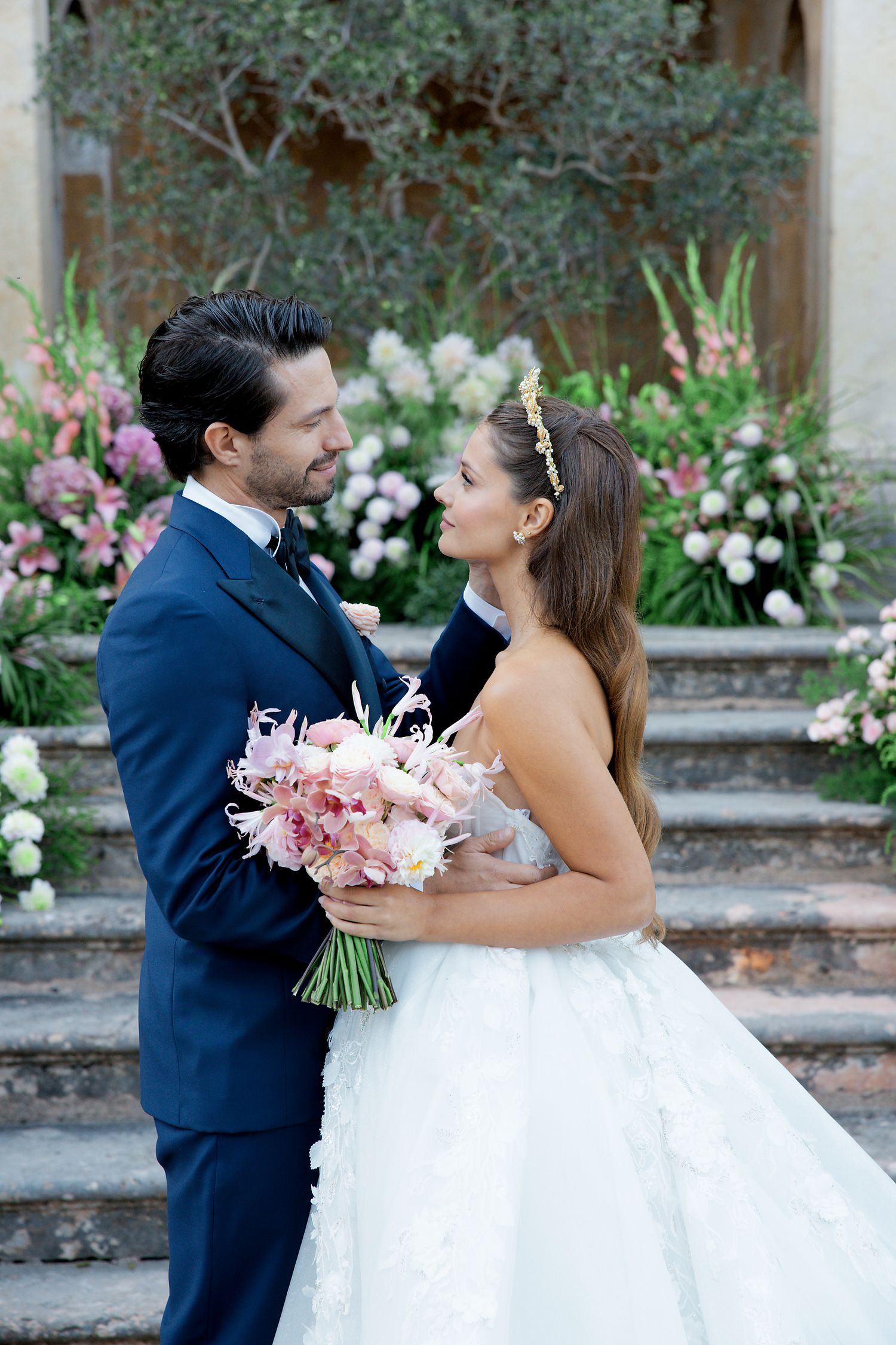 Couple sharing intimate moment on garden steps surrounded by pink and white flowers.