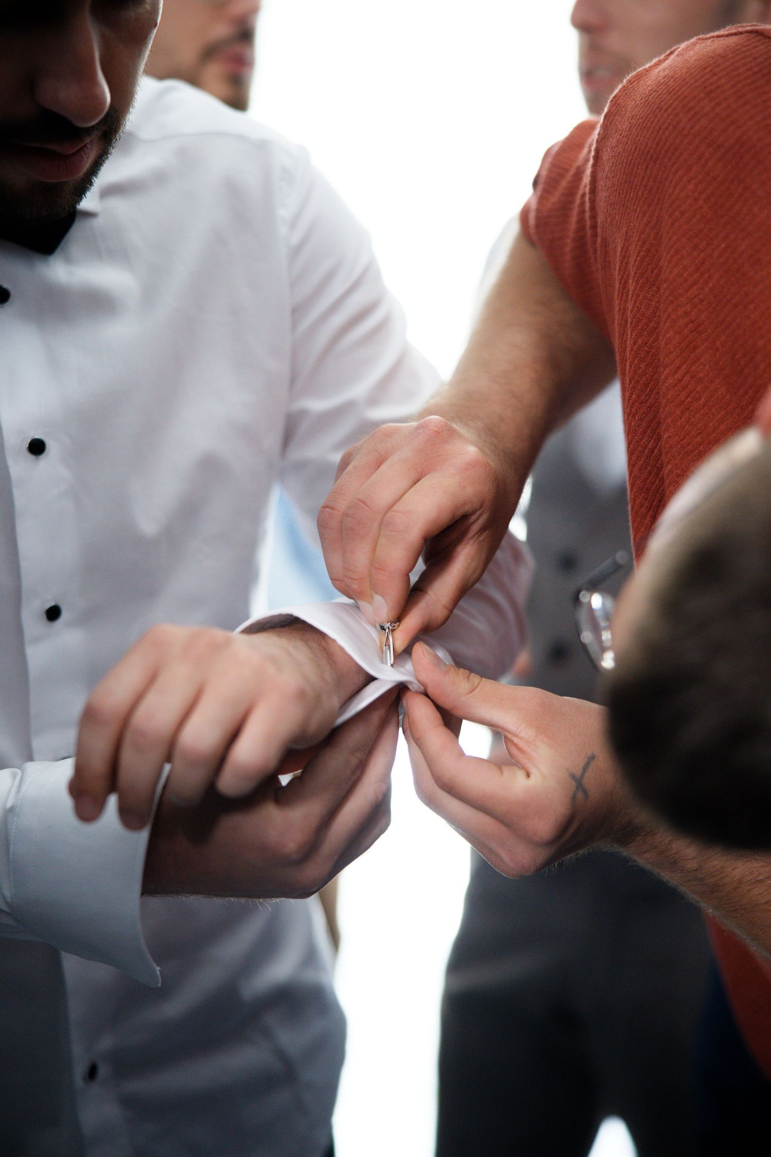 Hands help fasten cufflinks on a formal white dress shirt during wedding preparations.