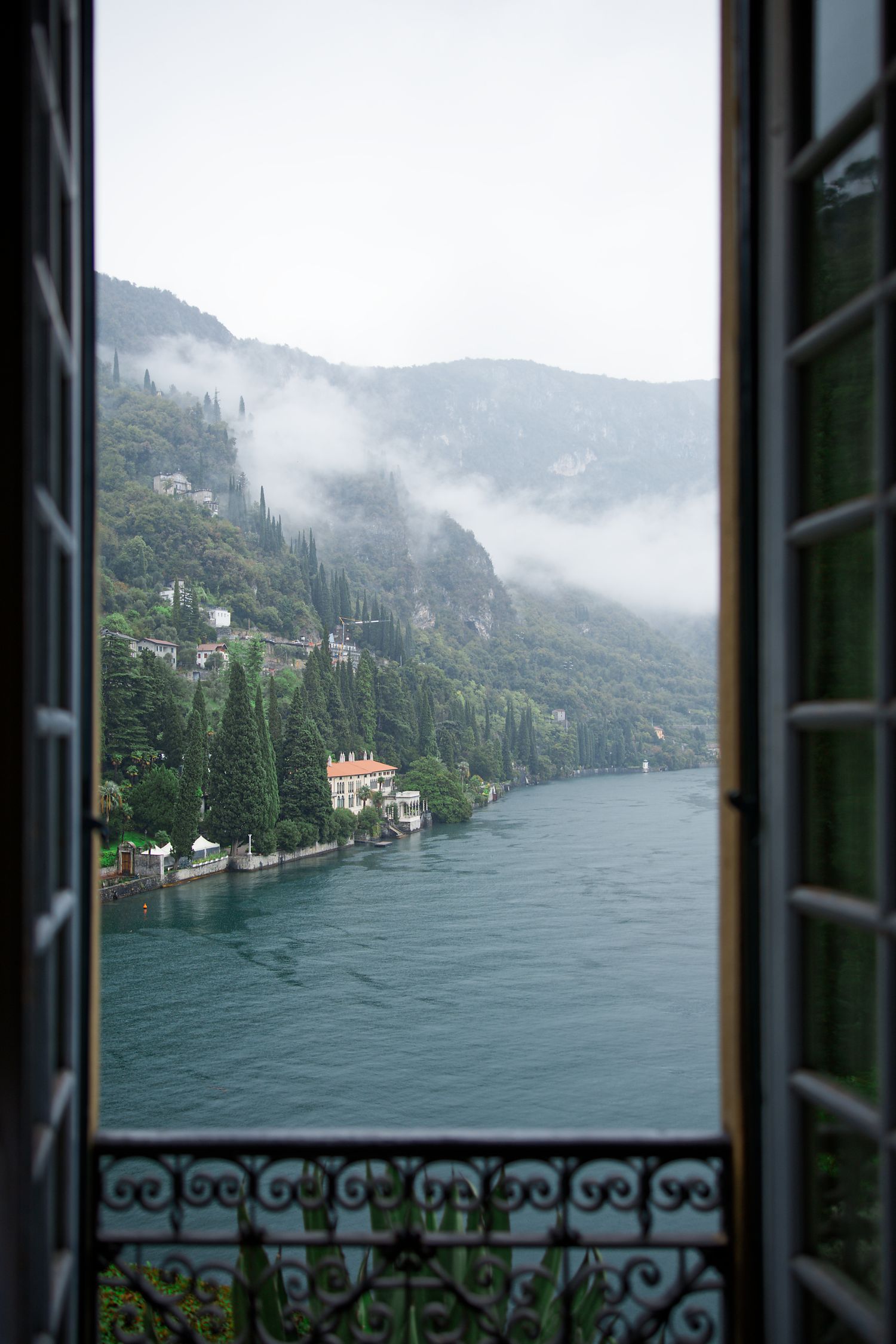 Misty lake view through an elegant wrought iron window frame in the Italian mountains.