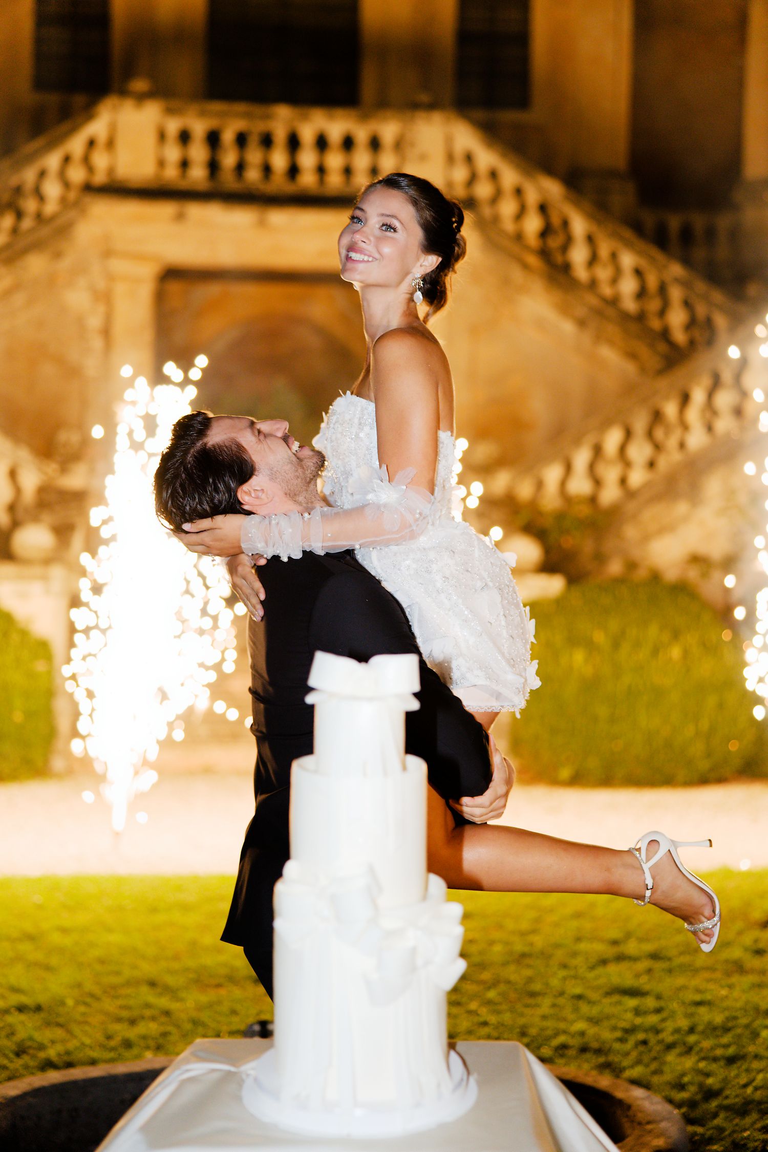 Playful wedding cake moment with sparklers in the background.