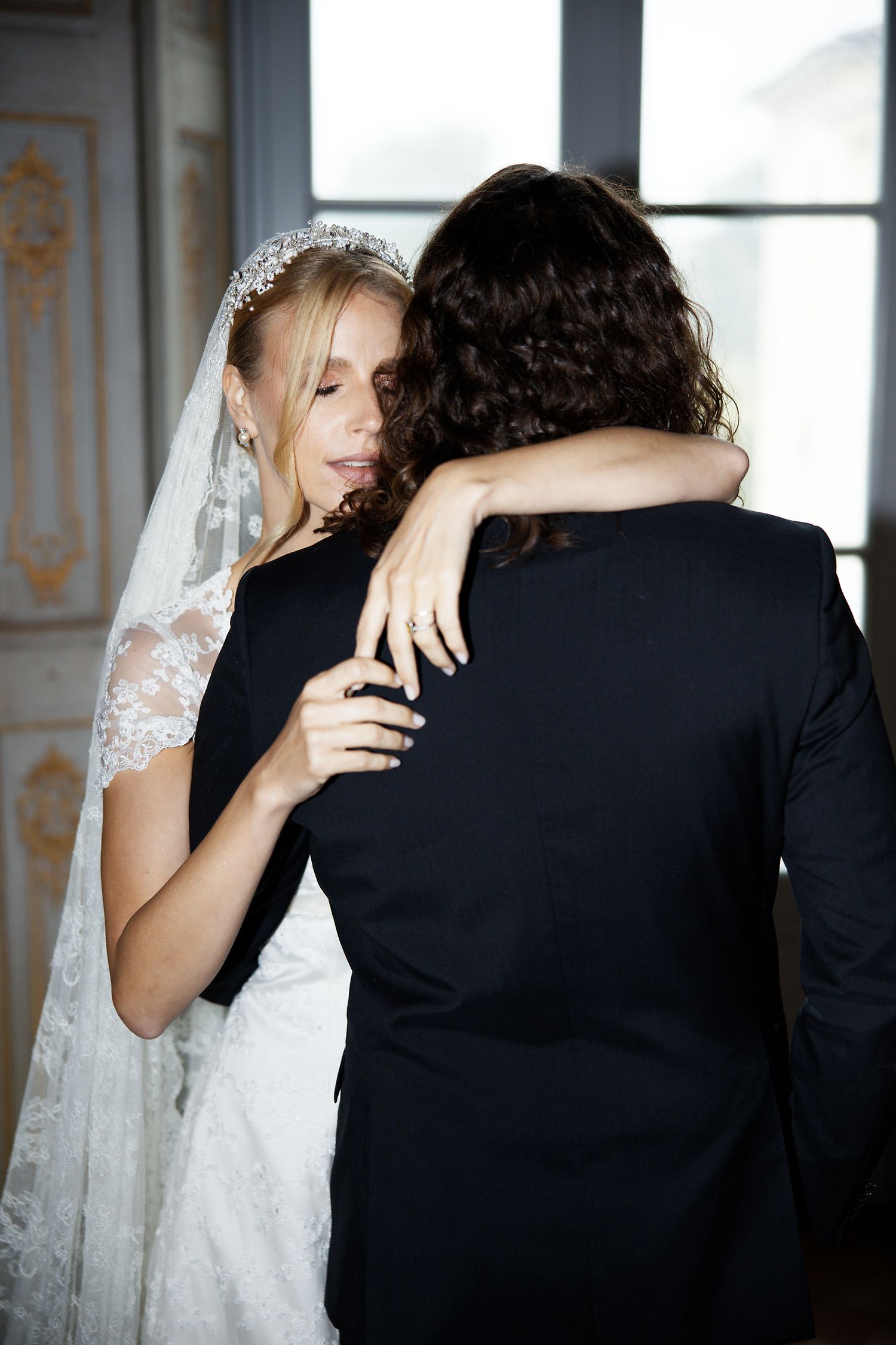 A couple shares an intimate embrace during their wedding, with the bride wearing a delicate lace veil and white gown.