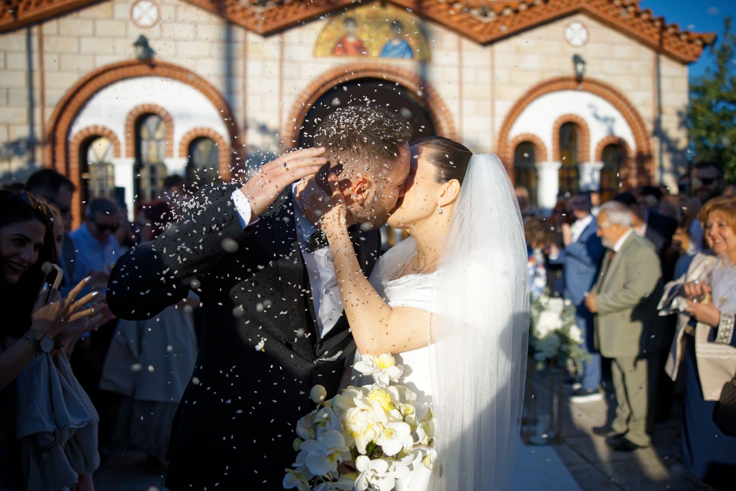 Newlyweds share first kiss outside church as guests shower them with confetti.