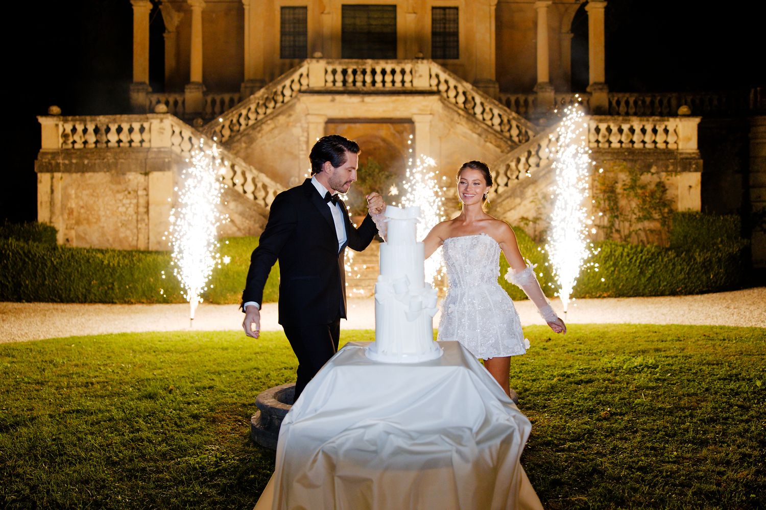 Night wedding celebration with fireworks display in front of grand villa.
