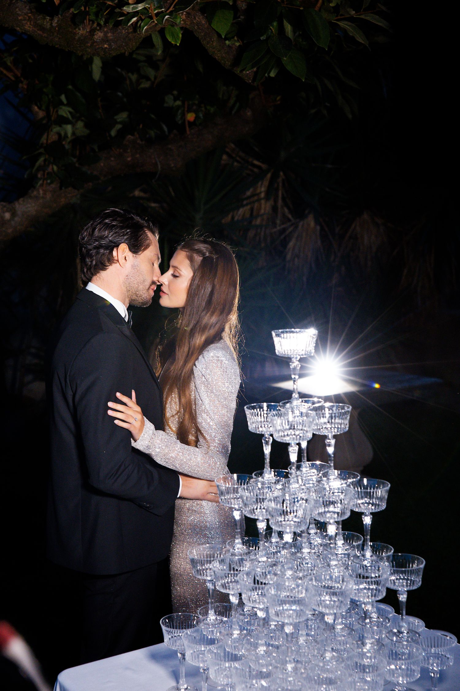A romantic moment captured at a wedding reception next to an elegant champagne tower glowing in the dark.