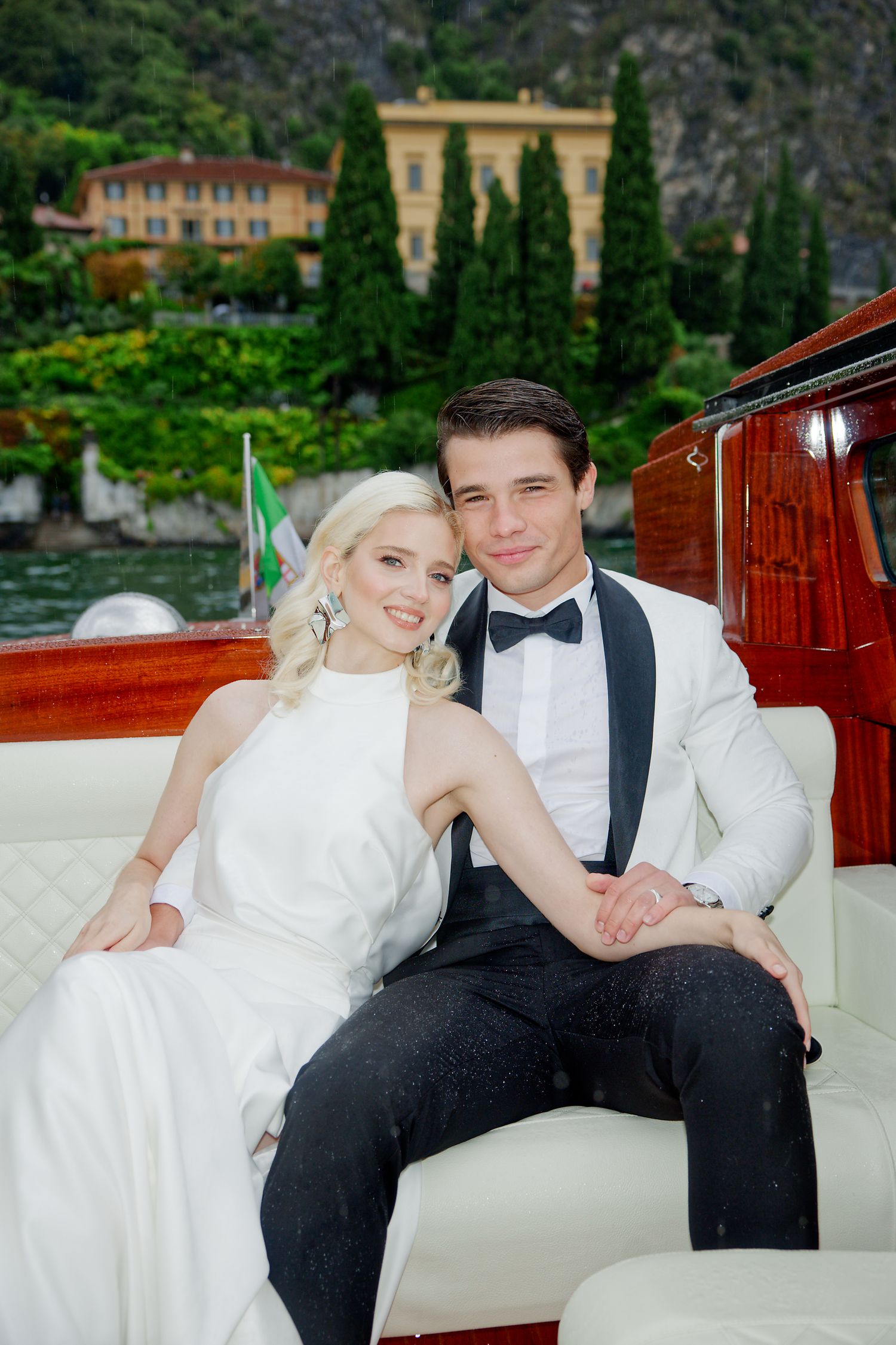 Elegant newlyweds share an intimate moment aboard a wooden boat against an Italian lakeside backdrop.