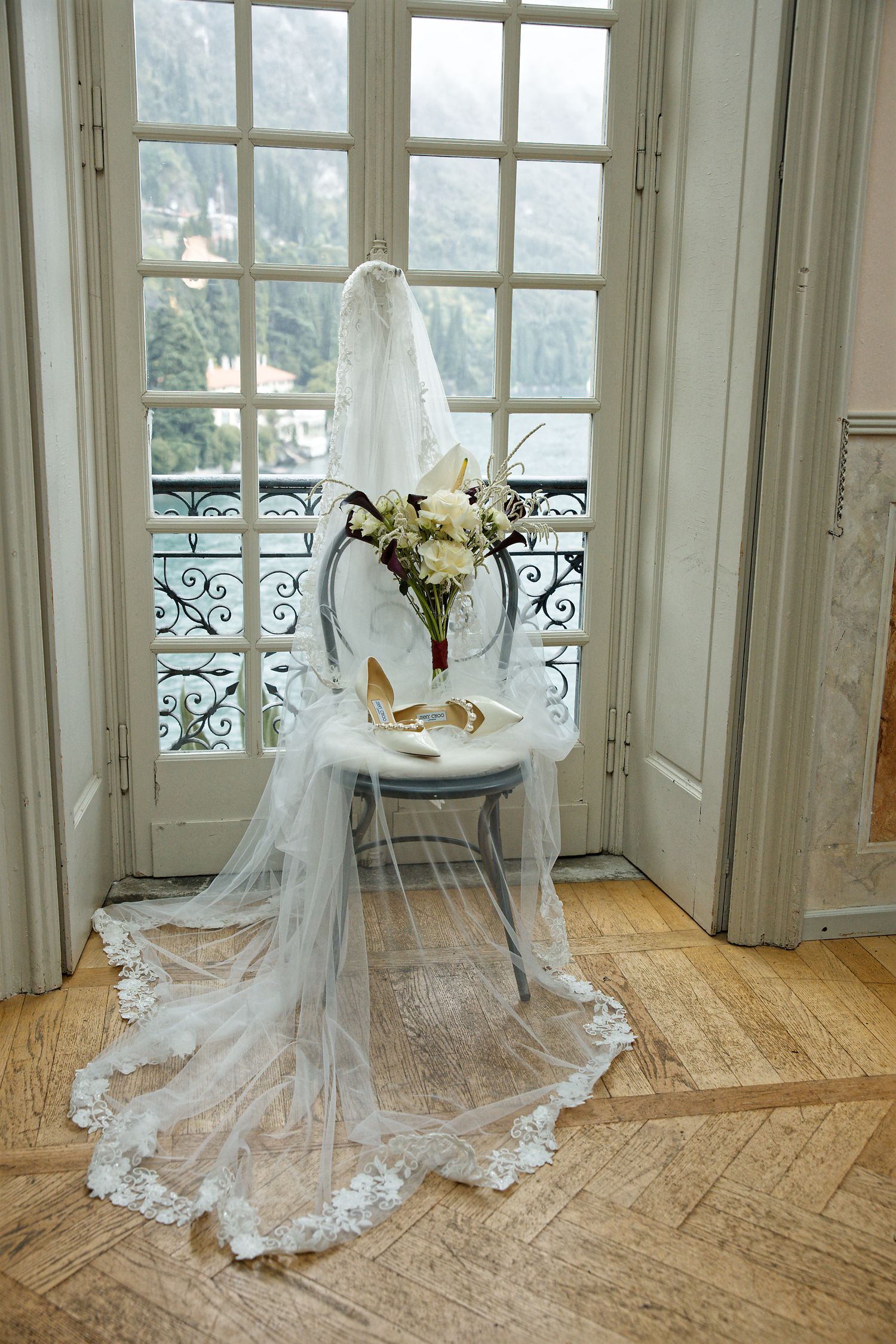 Wedding dress and veil displayed by window with lake view and floral arrangement.