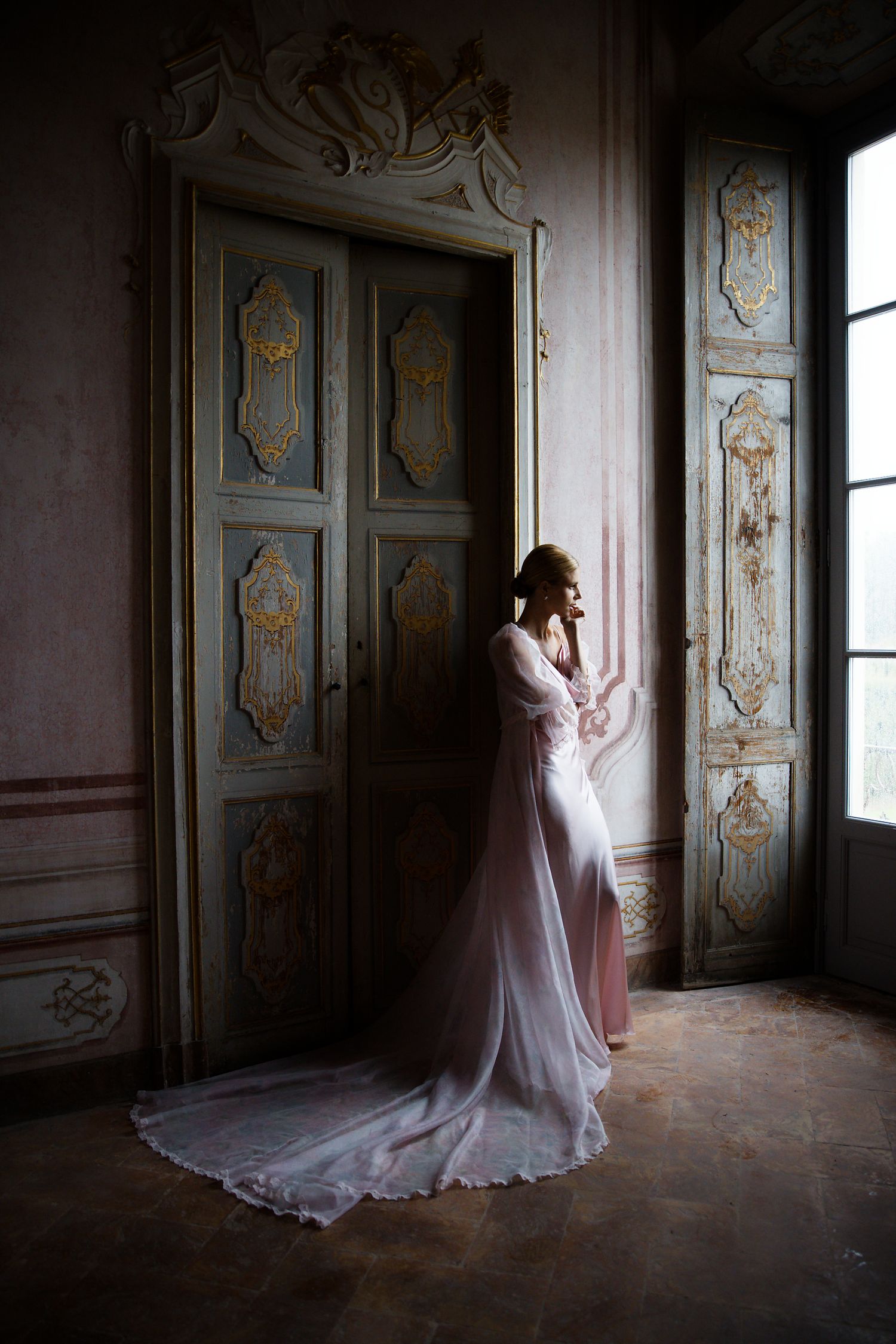 Romantic silhouette of bride in flowing gown against ornate vintage doorway and window.