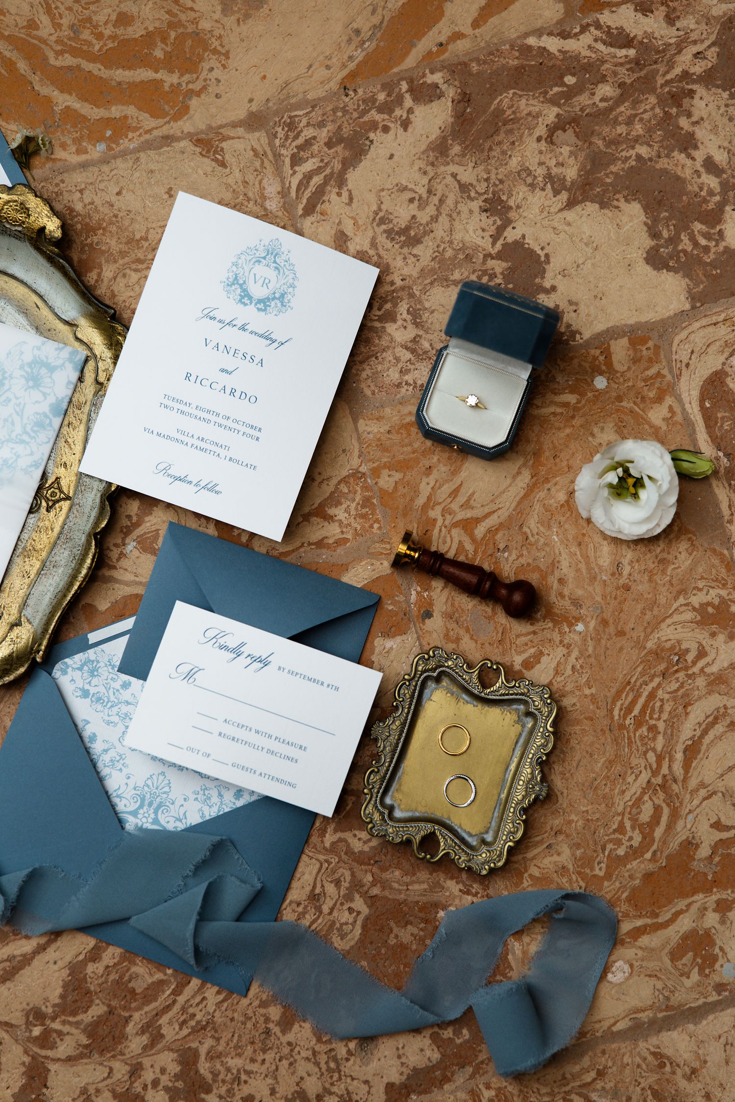 Wedding stationery flat lay with navy envelopes, antique frames and ring box on marble surface.