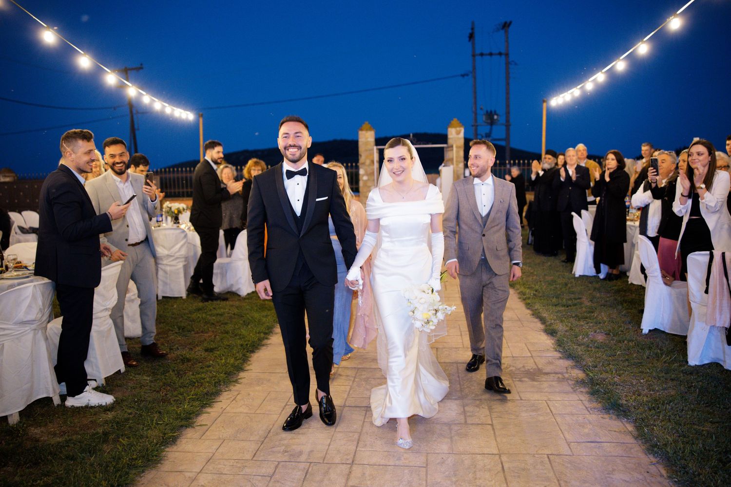 Outdoor evening wedding venue illuminated by string lights against a deep blue sky.