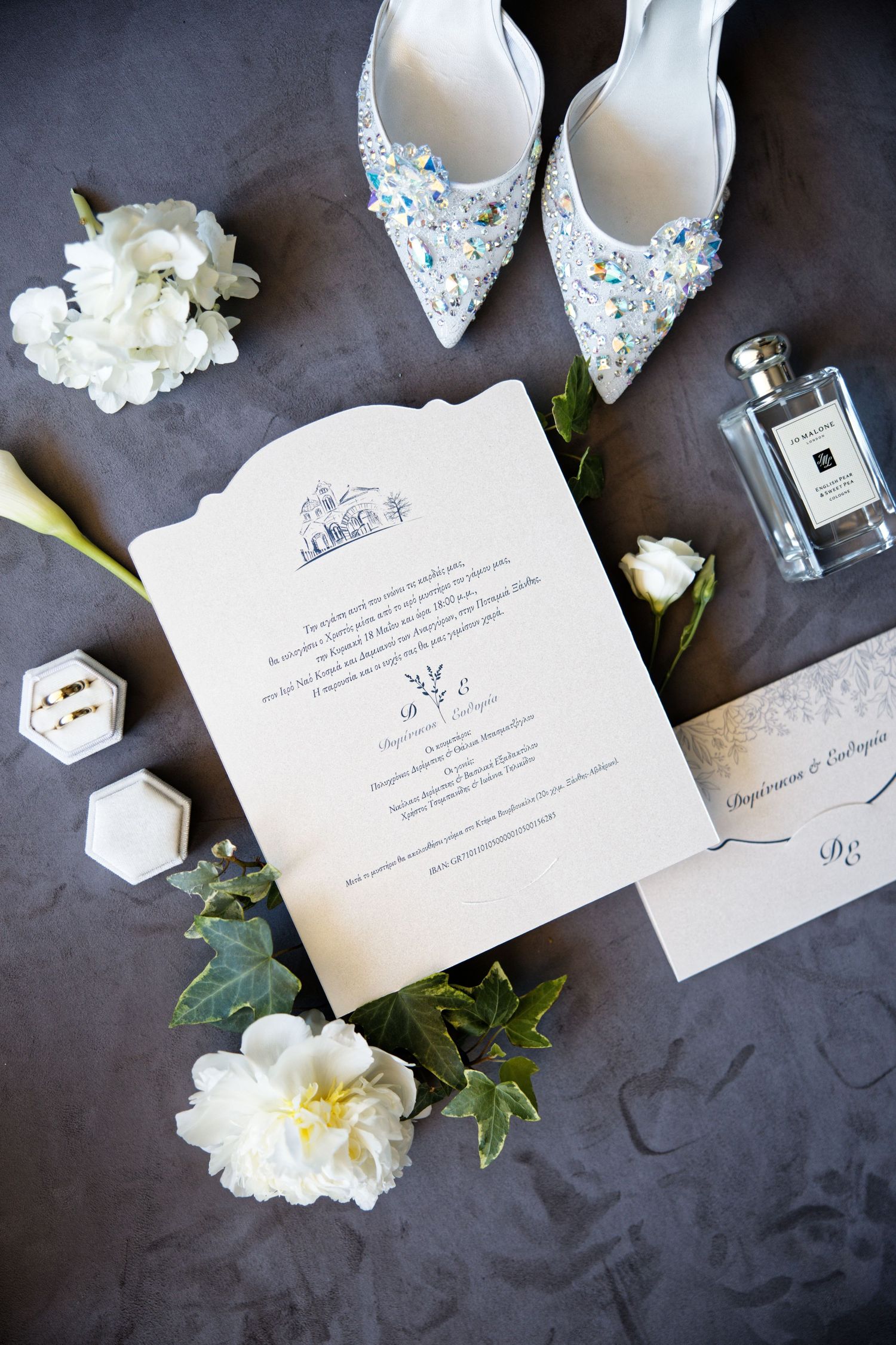 Wedding invitation suite styled with crystal shoes, perfume bottle and white flowers.