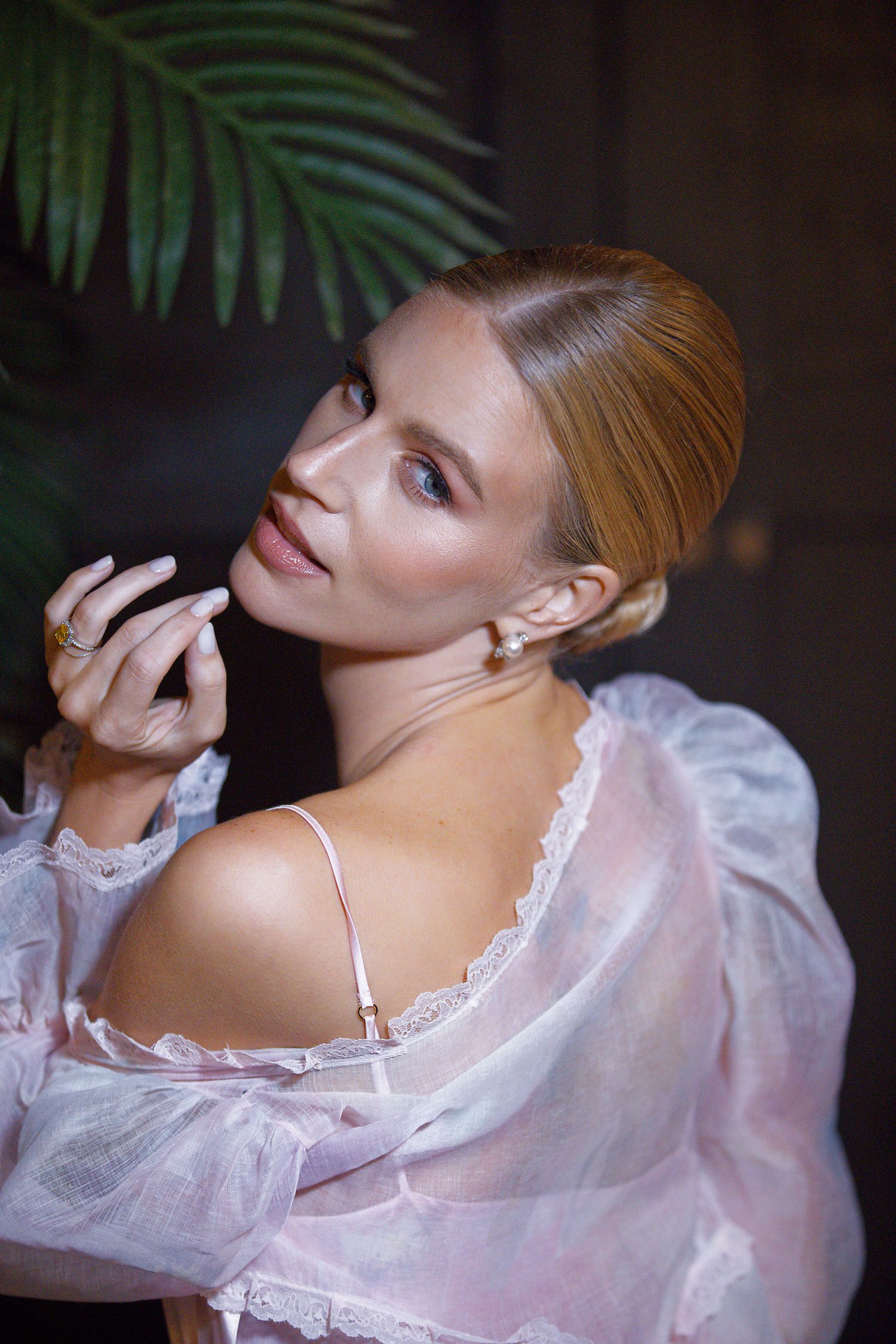 A romantic portrait showing a person in a sheer pink lace robe looking over their shoulder with palm fronds in background.