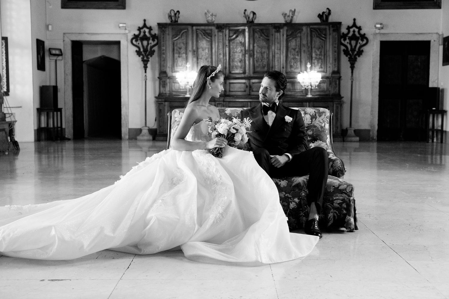Black and white wedding photo of couple posing in grand ballroom with ornate wooden decor.