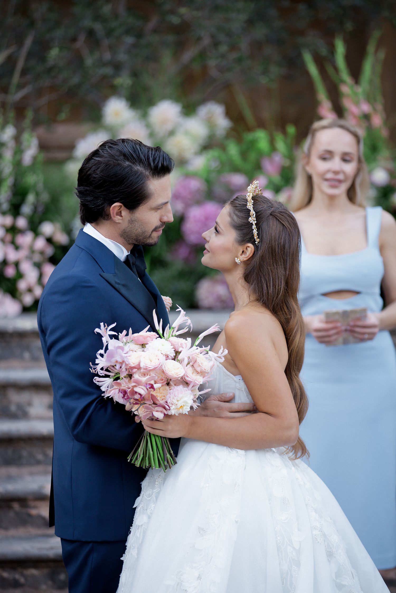 Wedding moment captured in garden setting with pink floral bouquet and light blue bridesmaid dress.