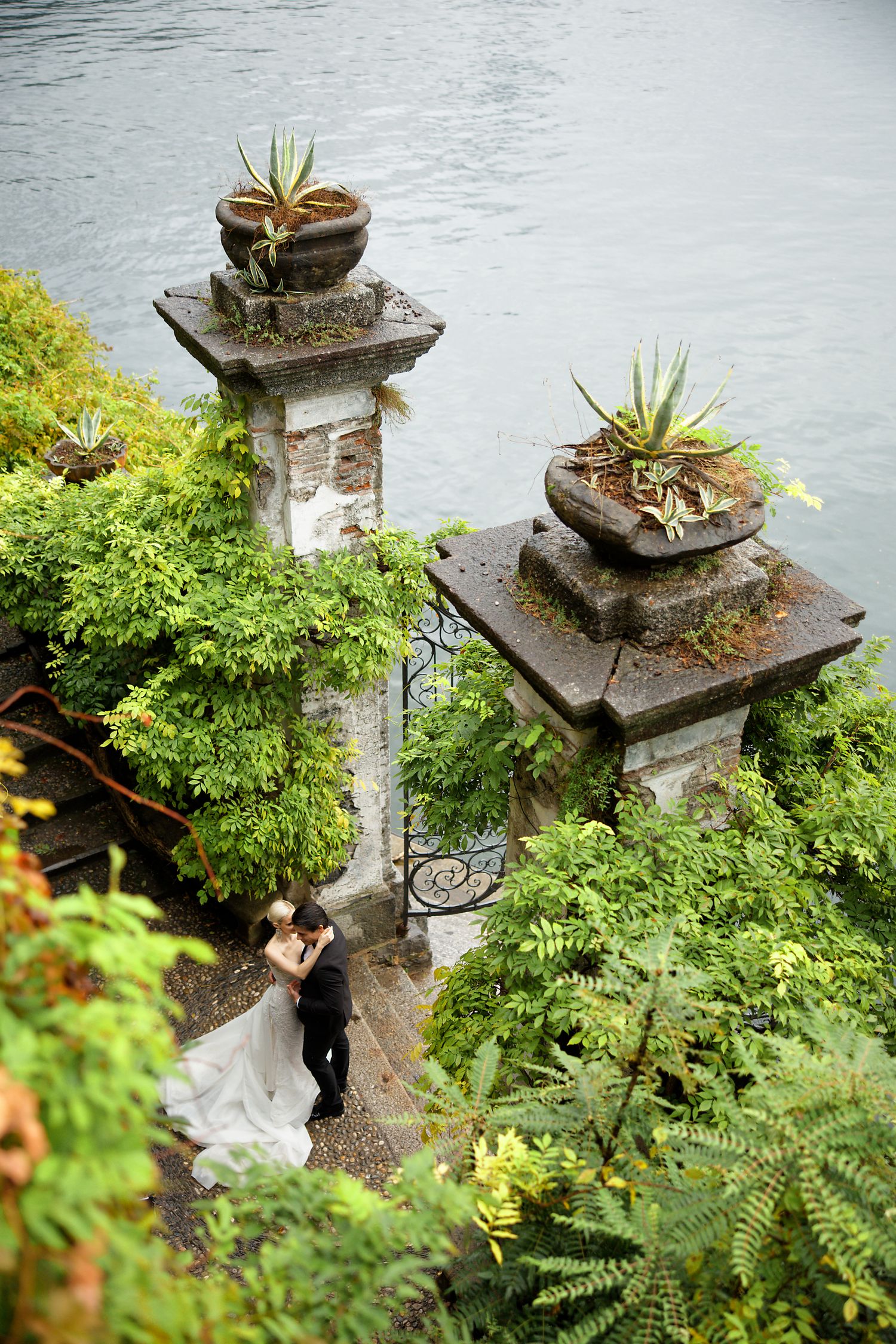 Stone pillars with succulents frame a garden path overlooking a serene lake.