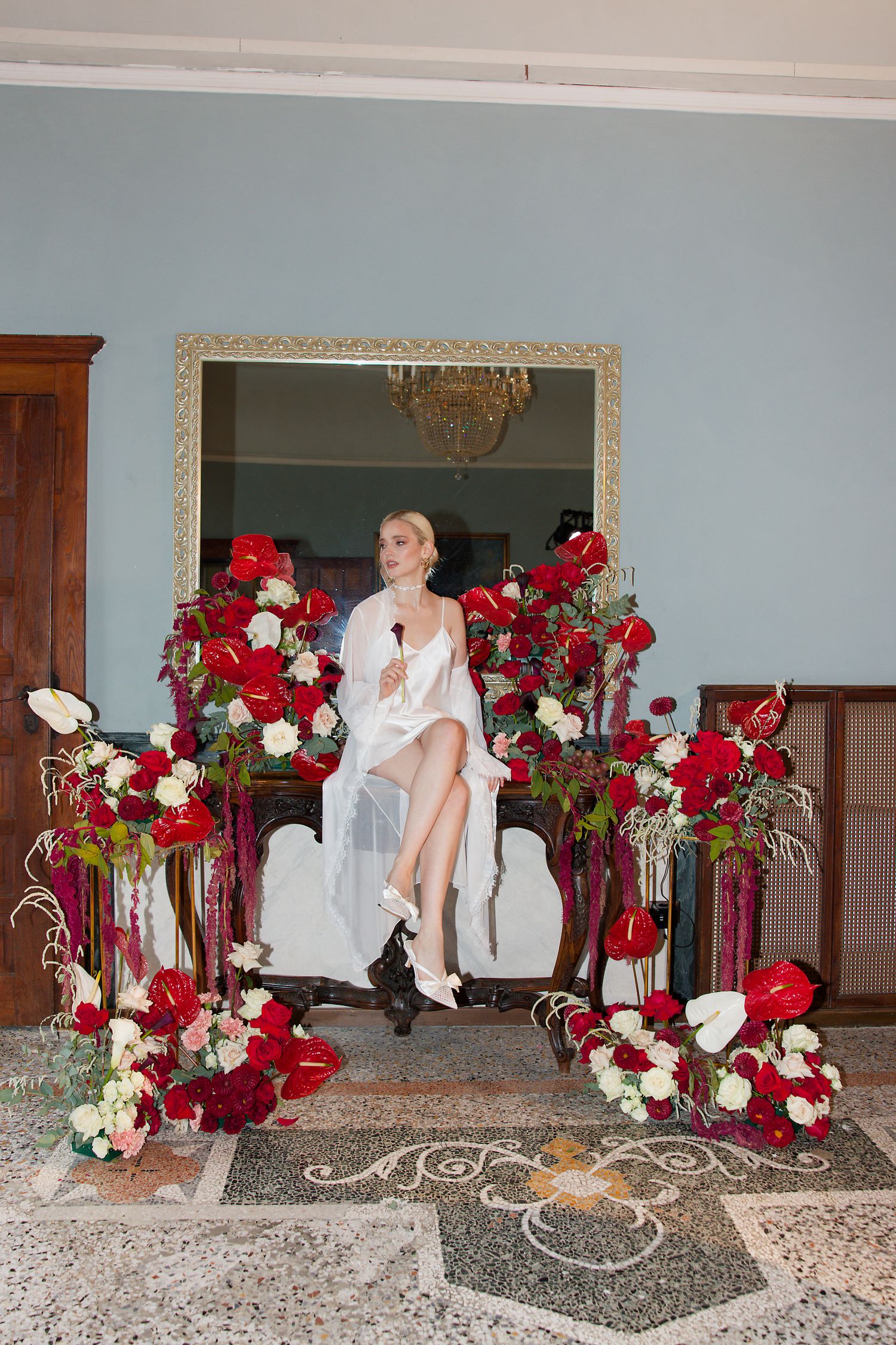 Elegant bridal scene with dramatic red and white rose floral arrangements framing an ornate mirror and chair setup.
