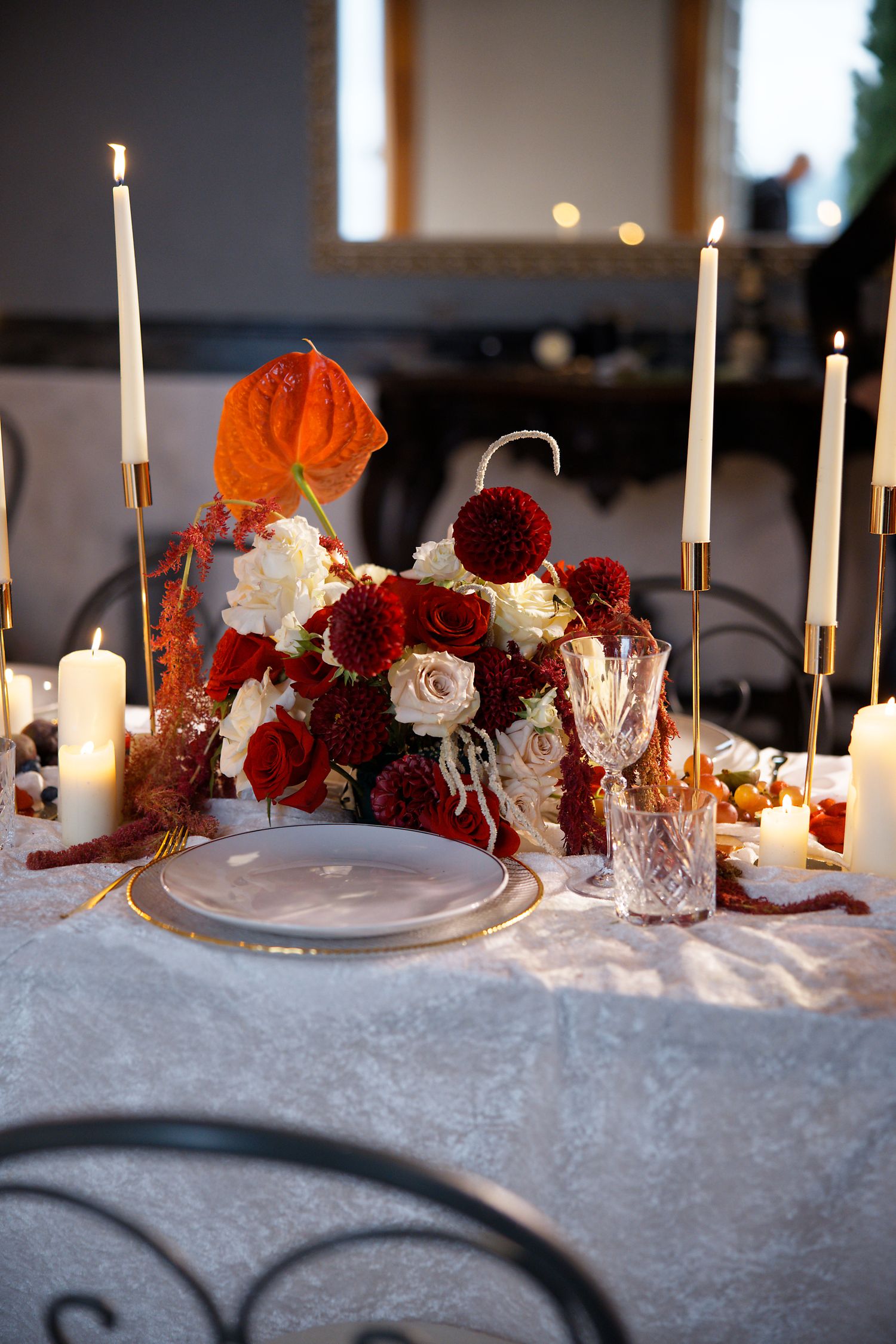 Romantic table setting with red and white flowers, candles, and crystal glassware on white linen.
