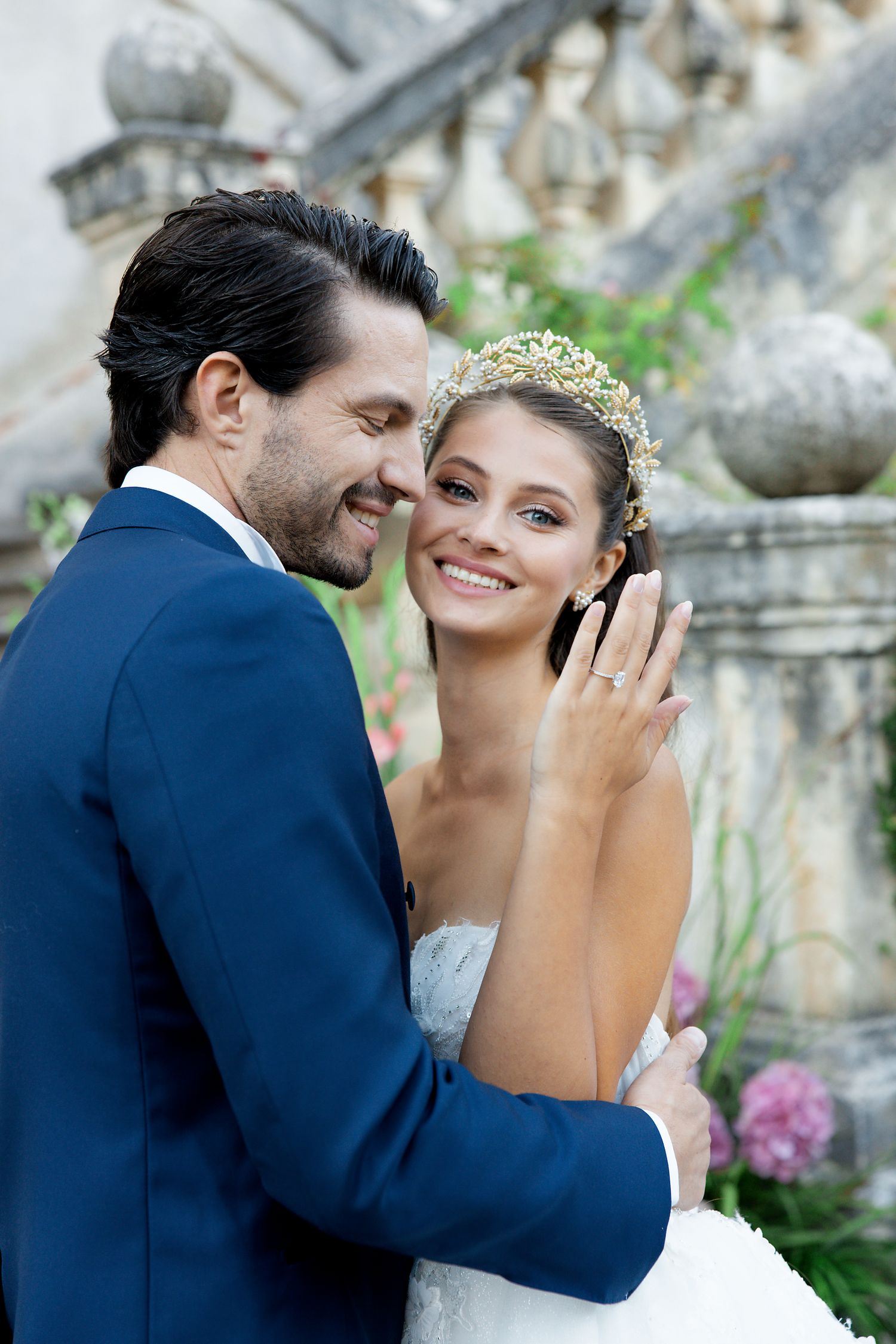 Couple shares a beautiful moment at their wedding, with the bride wearing a delicate tiara and groom in a navy suit.