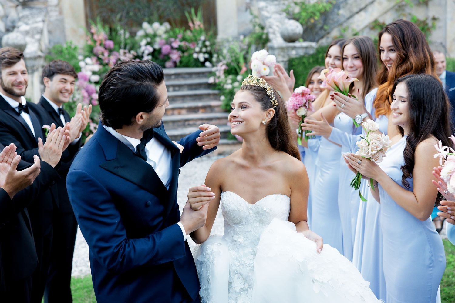 Wedding celebration in a garden with guests wearing formal attire and light blue dresses.