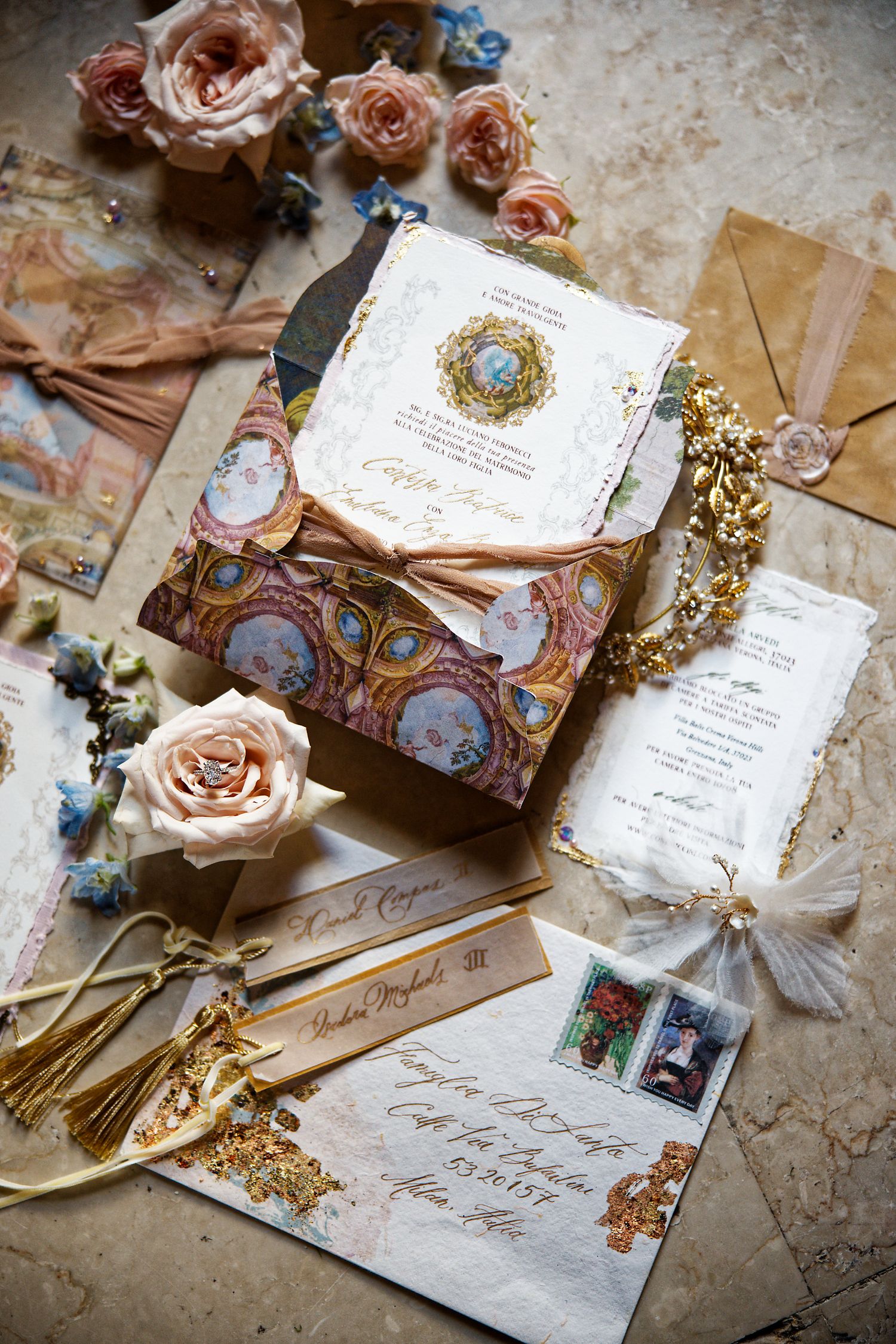 Elegant wedding stationery with vintage floral design, roses, and gold accents arranged on textured surface.