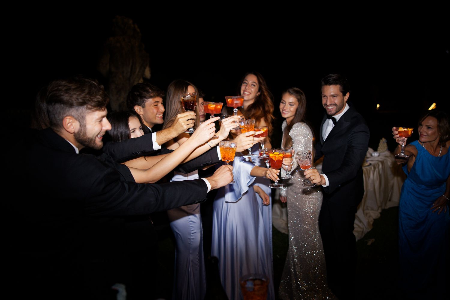 Wedding celebration with guests toasting at a nighttime outdoor party.